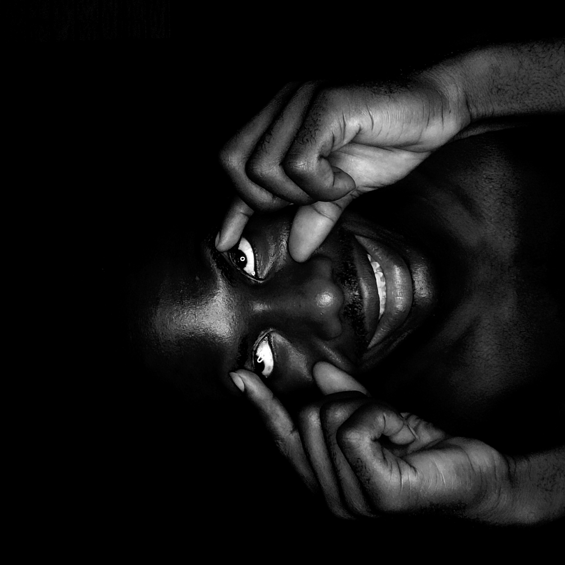 A black and white close-up image shows a person with dark skin looking directly at the viewer. The person is smiling, exposing their teeth, and using their fingers to pull their eyelids up and open. The person's face is the main focus of the image. The location is not discernible from the image, therefore no information regarding Narayi, Nigeria can be made.
