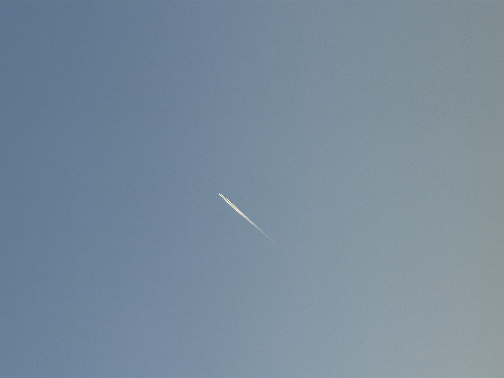 A contrail is visible in the blue sky. The photograph was taken in Gošići, Montenegro.