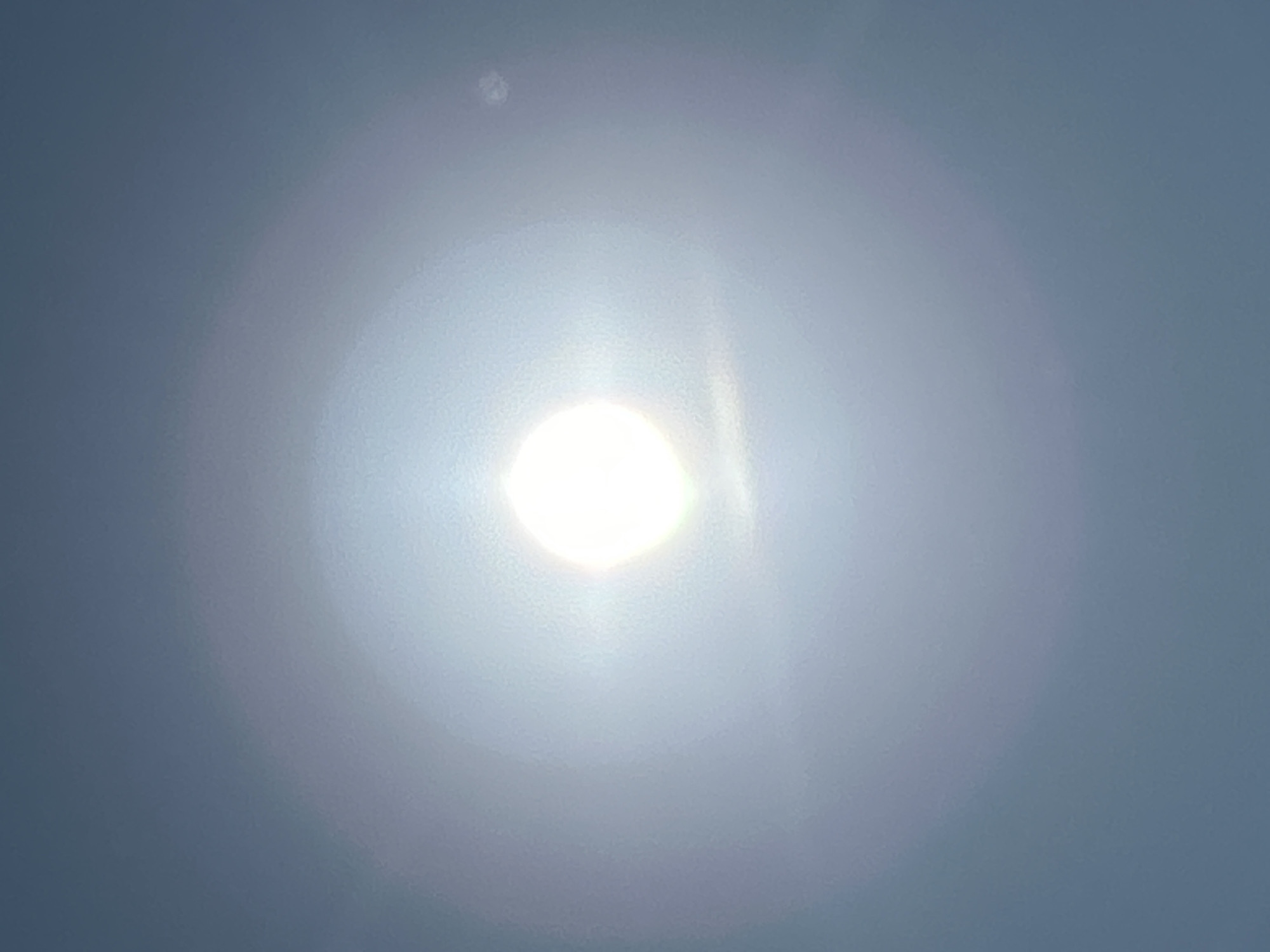 This is a photograph of the sun taken outdoors in Matraevo, Russia. The sun is bright and centrally located in the frame, with a halo of light surrounding it. The sky is clear and blue, with no clouds visible. The image appears to have been taken on a sunny day, with no indication of any people or other objects in the vicinity. The overall impression is one of a clear, bright day with the sun dominating the sky.