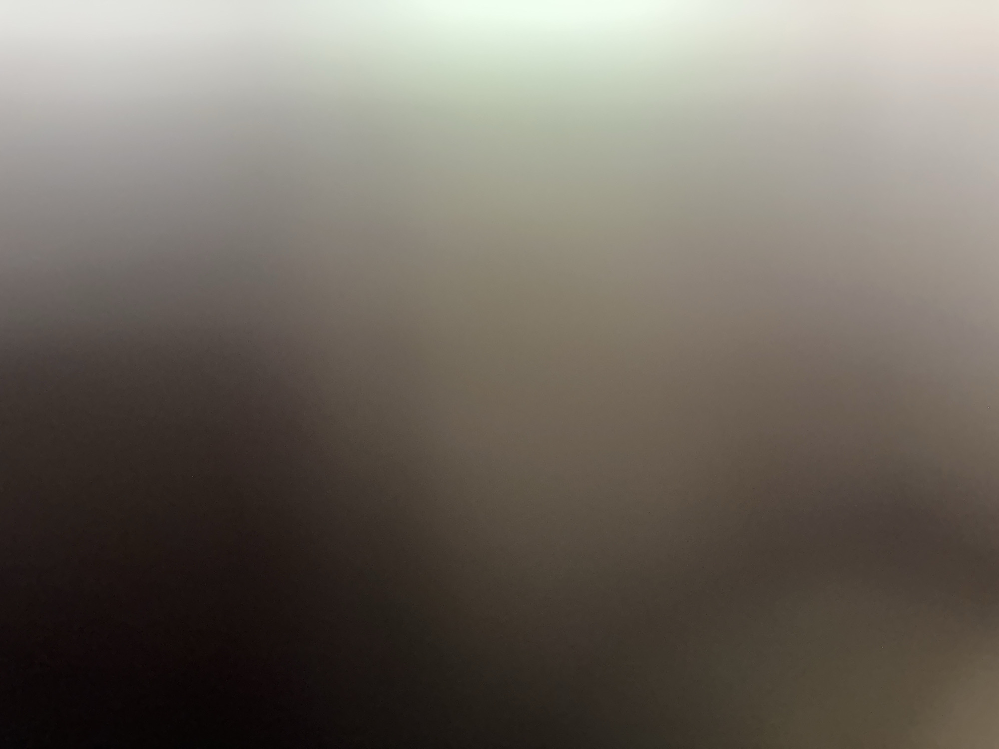 This is a blurred, abstract image that appears to be a photograph with a gradient of color. The top of the image is bright white, fading into a light gray, then a darker gray, and finally a deep black at the bottom. There are no discernible subjects, objects, or scenes. The image does not depict any activity or event. There are no notable details such as time of day, weather, location cues, or emotions, as the image is entirely abstract. There is no visible text.