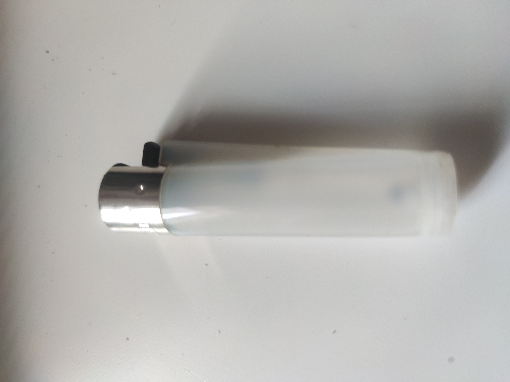 A translucent white lighter rests on a white surface. The lighter has a silver top and a black switch. The background is out of focus. The location is unknown.