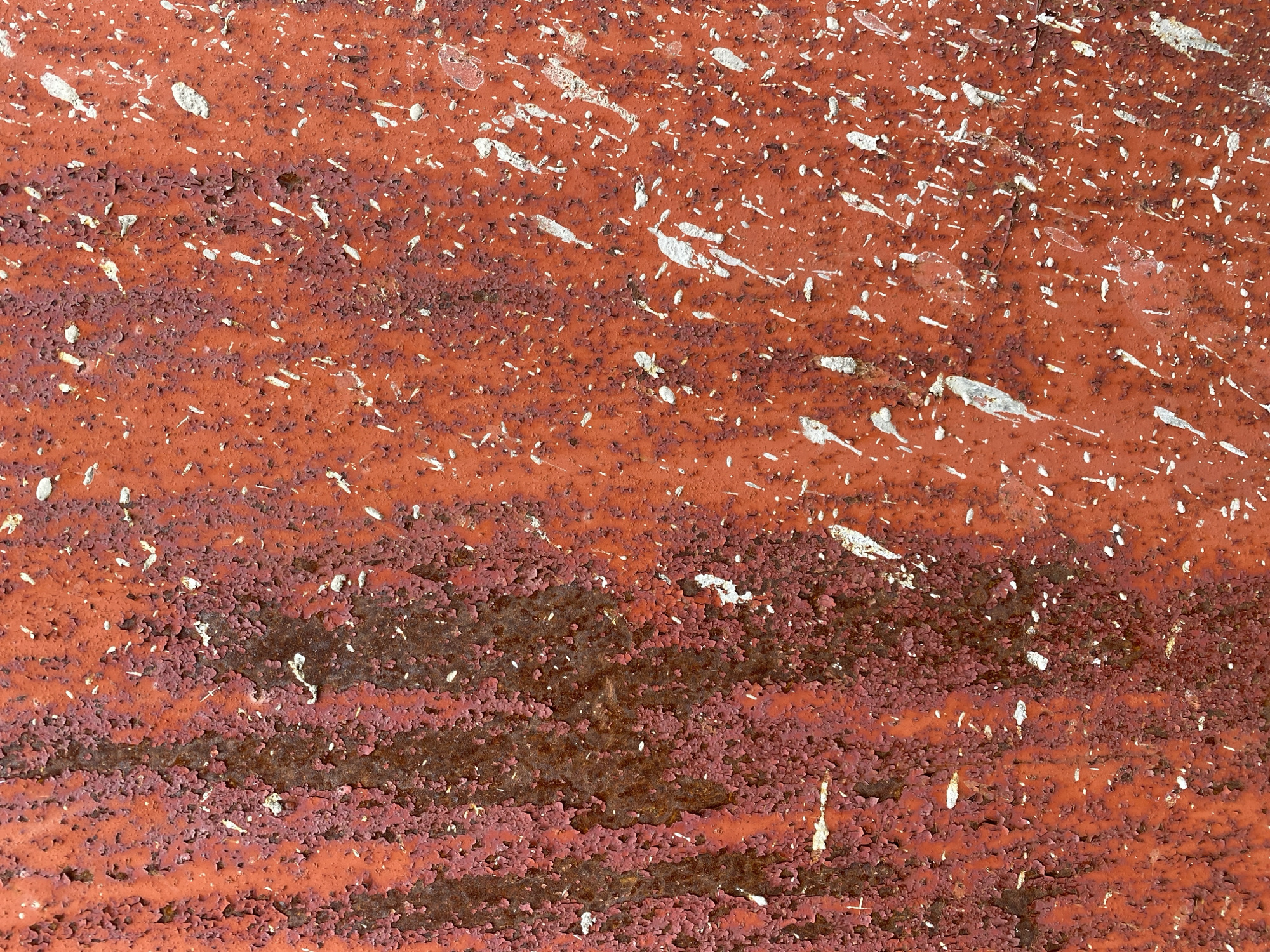 This is a close-up, full-frame, flat lay photograph of a weathered, orange-red, rusty metal surface. The surface is characterized by peeling paint and scattered white splatters. The texture is rough and uneven, with areas of exposed rust. There are no people, animals, or identifiable objects present. The location in Vitsebsk, Belarus cannot be determined from the image itself.