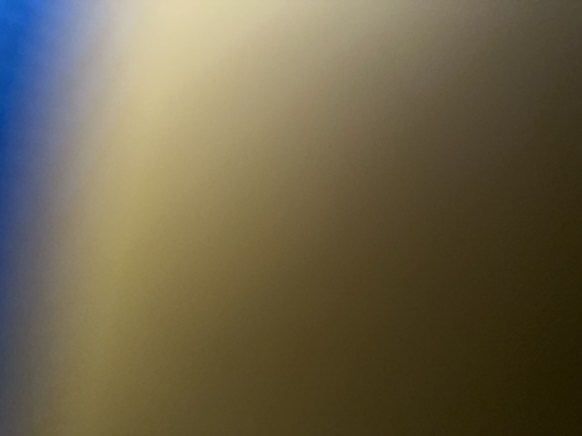 The image is an abstract, out-of-focus shot featuring a gradient of colors. On the left side, there's a strong band of deep blue that gradually fades into a lighter, desaturated blue. This transitions into a broad swath of light beige or cream, which then softly darkens to a muted olive green and finally to a deep brown or dark grey on the right side.
The lighting appears to be dim and diffused, creating a smooth, atmospheric blend of colors without sharp lines or distinct forms. There are no discernible subjects, objects, people, or specific scene elements visible. The texture of the surface, if any, is obscured by the blur, though some very subtle graininess is present. The overall impression is that of an abstract color study or a photograph of a soft, shifting light source. Without any contextual elements, it's impossible to determine the time of day, weather, or specific location, although the provided context of "Belgrade, Serbia" does not offer any visual clues within the image itself. No text is visible.
