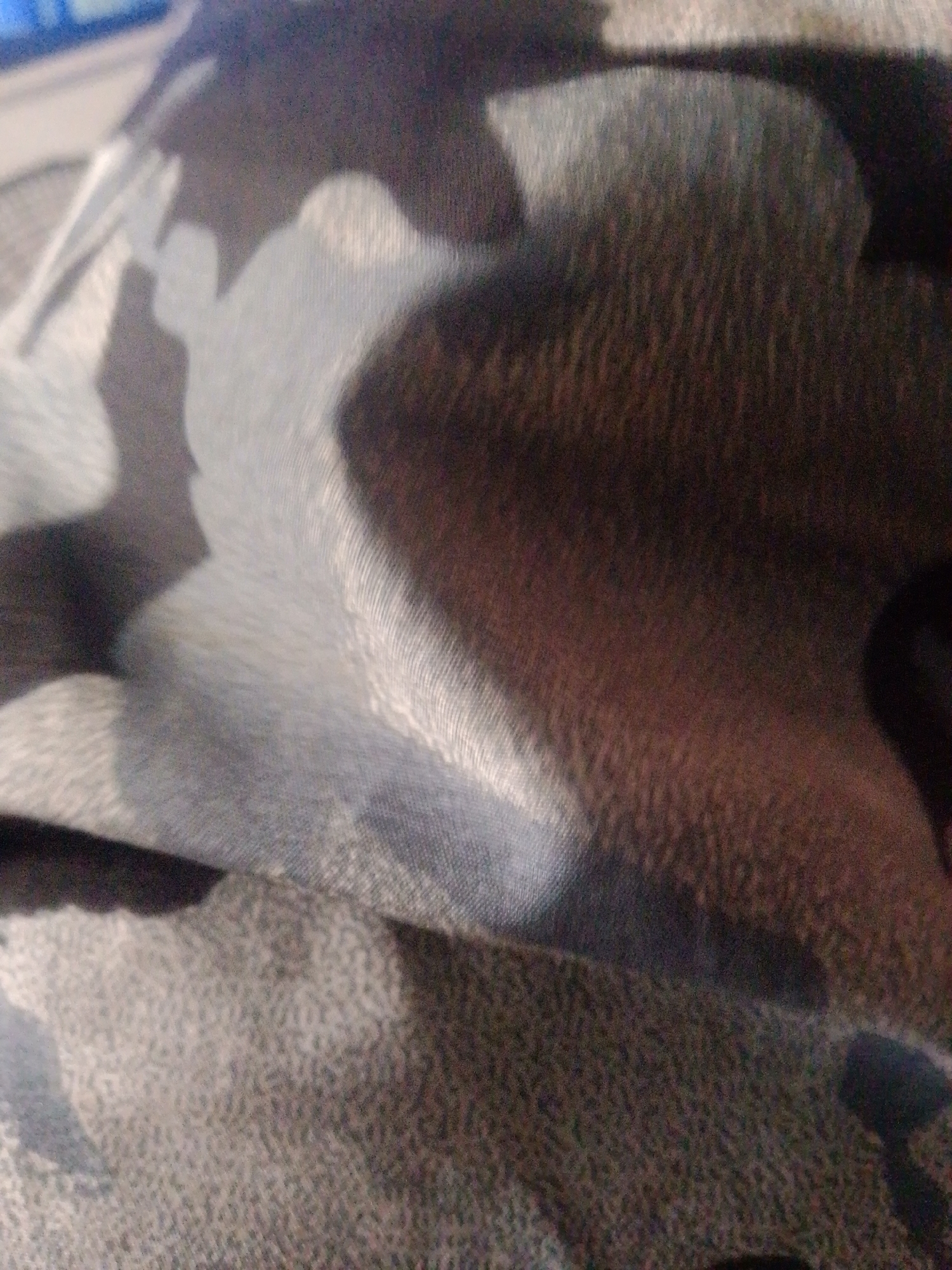 The image shows a close-up of a patterned fabric with colors ranging from light gray to dark brown and black. The pattern appears mottled or camouflage-like. The fabric is textured with a fine, granular appearance. There is no information about the location in the city of Juan Griego, Venezuela, and no people, subjects, objects, actions, interactions, or environment are visible beyond the fabric itself.