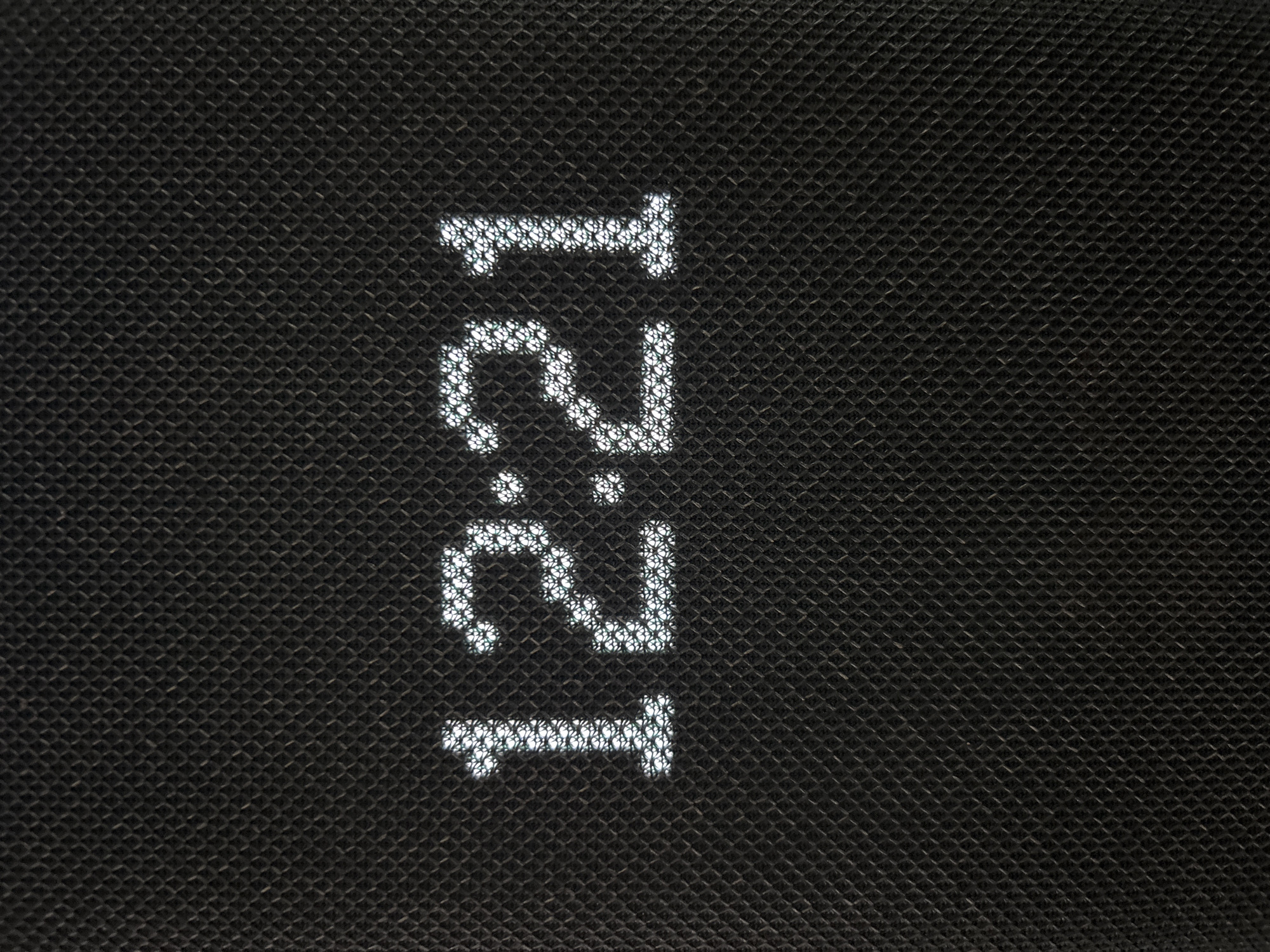 The image shows a digital display of the time "12:21" on a black textured surface. The digits are formed by small white lights. The texture of the surface appears to be a fabric or woven material with a repeating diamond pattern. There are no people or any other discernible objects in the image. The location in the city of Arkhipovskoye, Russia, is not discernible from the image itself.