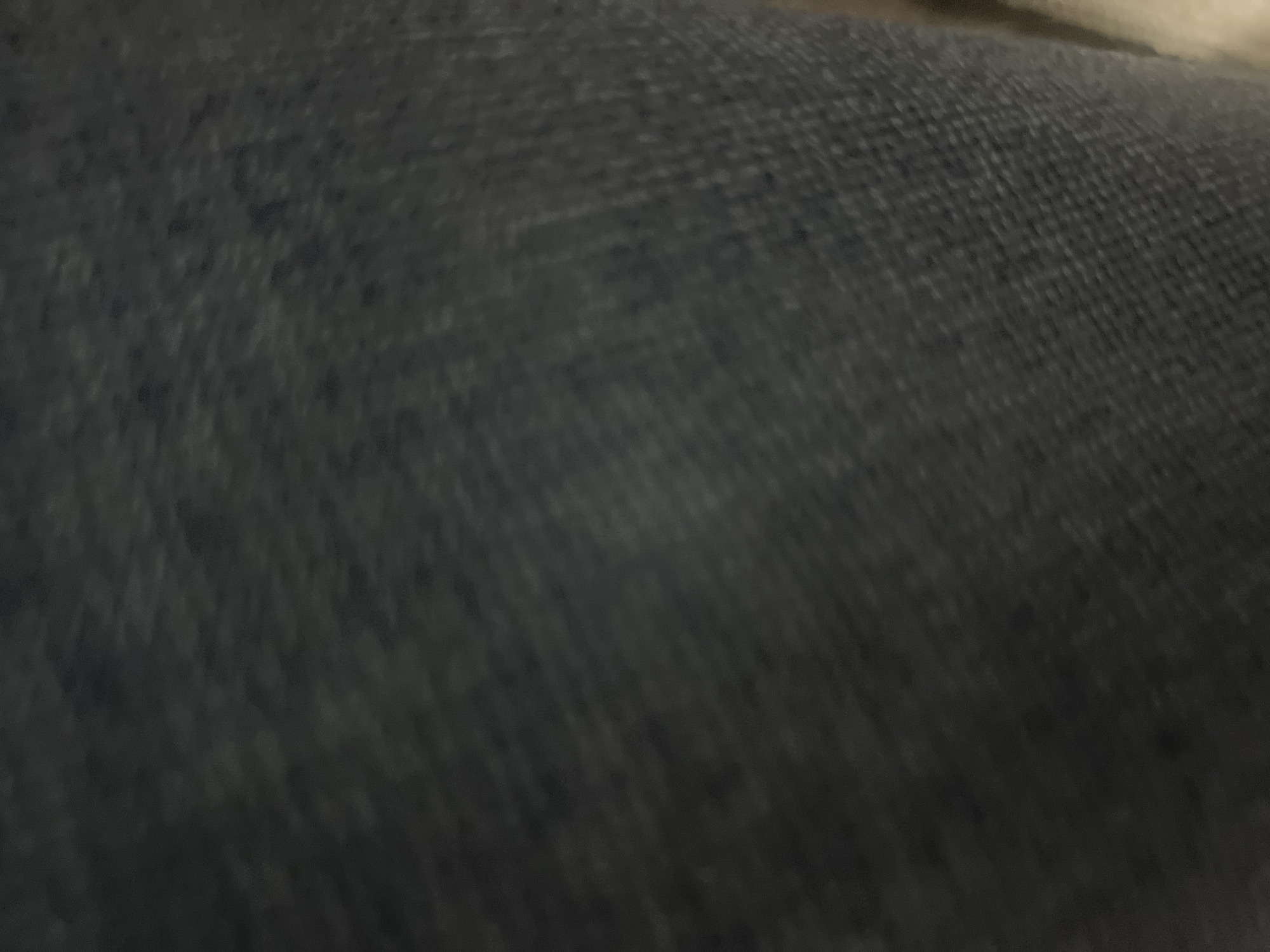 The image shows a close-up, abstract view of dark blue denim fabric. The texture of the woven material is visible, with a slightly lighter, faded area in the center. The lighting is dim, casting shadows and creating a textured, somewhat blurred effect. There are no discernible objects, people, actions, interactions, or environmental elements identifiable within this close-up of fabric. Therefore, it is not possible to determine any location, including in the city of Casablanca, Morocco.