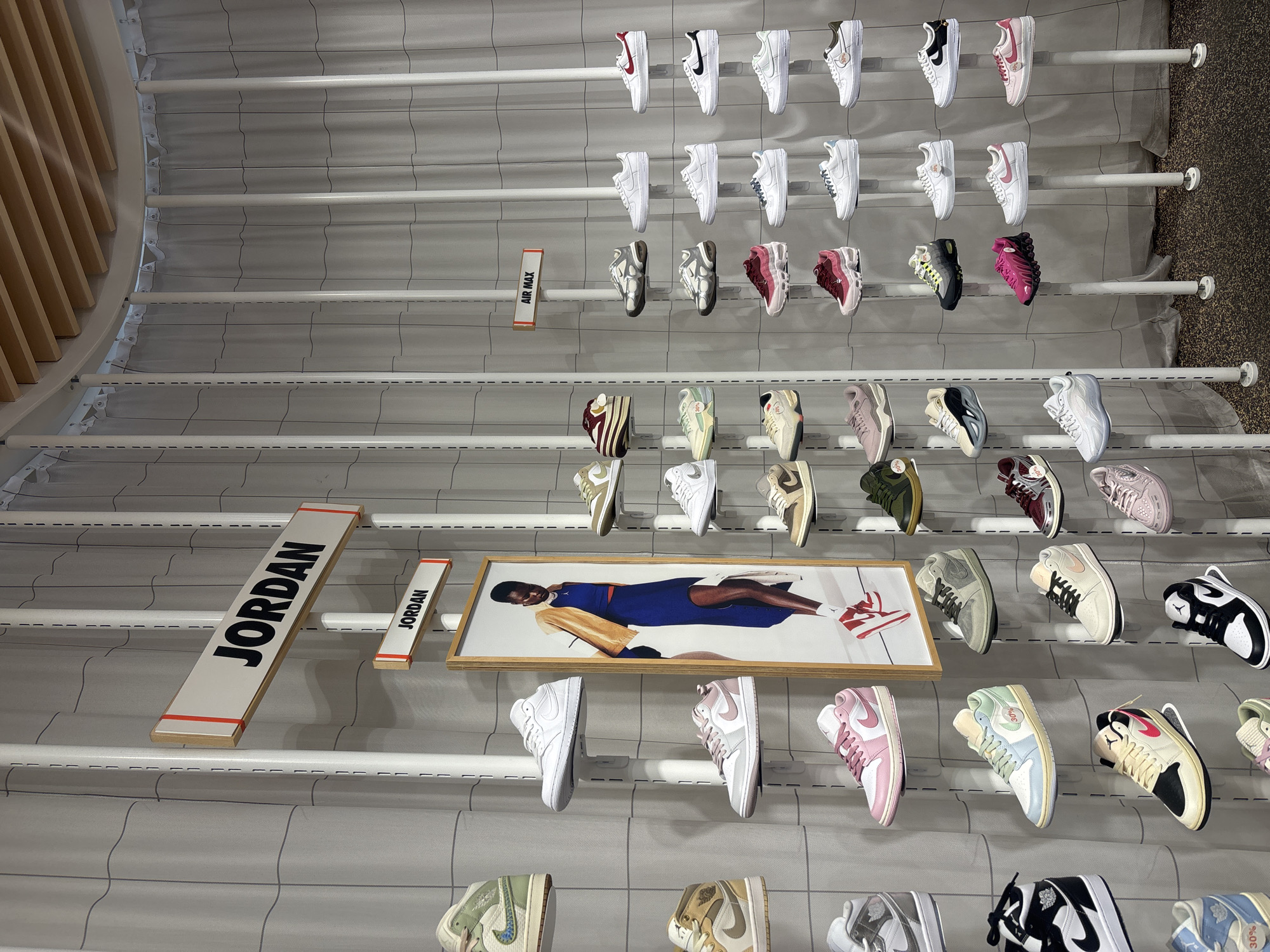 The image shows a display of sneakers on shelves at a store in Puebla, Mexico. The sneakers are predominantly Nike Air Force 1s and Air Jordan 1s. The shelves are white with a gray grid pattern in the background. There are signs labeling "Air Max" and "Jordan". A framed image of Michael Jordan is displayed.