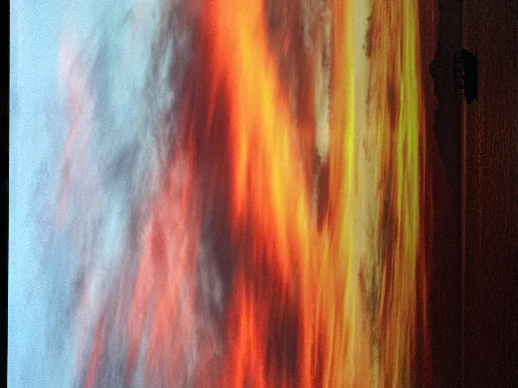 The image depicts a vibrant sunset over a body of water. The sky is a dramatic canvas of fiery reds, oranges, and yellows, with streaks of pink and blue. Wispy clouds are illuminated by the setting sun, creating a sense of depth and texture. In the distance, a dark silhouette of mountains or hills can be seen against the horizon. A small boat with a dark canopy is anchored on the water, adding a focal point to the scene. The water itself is dark and reflects the colors of the sky. There are no people visible in the image.
This image is not related to Saratov, Russia. The scene is a natural landscape, likely a coastal or lake area, and there are no urban elements visible that would suggest a specific city location.