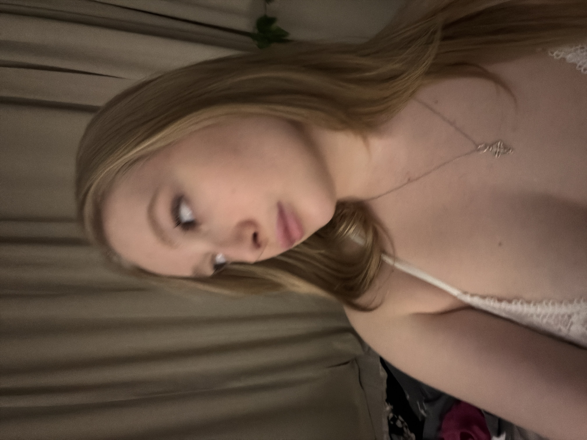 A person with long, light brown hair and fair skin is visible in the image. They are wearing a white top with lace details and a silver necklace with a pendant. The background features draped fabric in muted brown tones. The location, Rossiyskiy, Russia, is not discernible from the image.