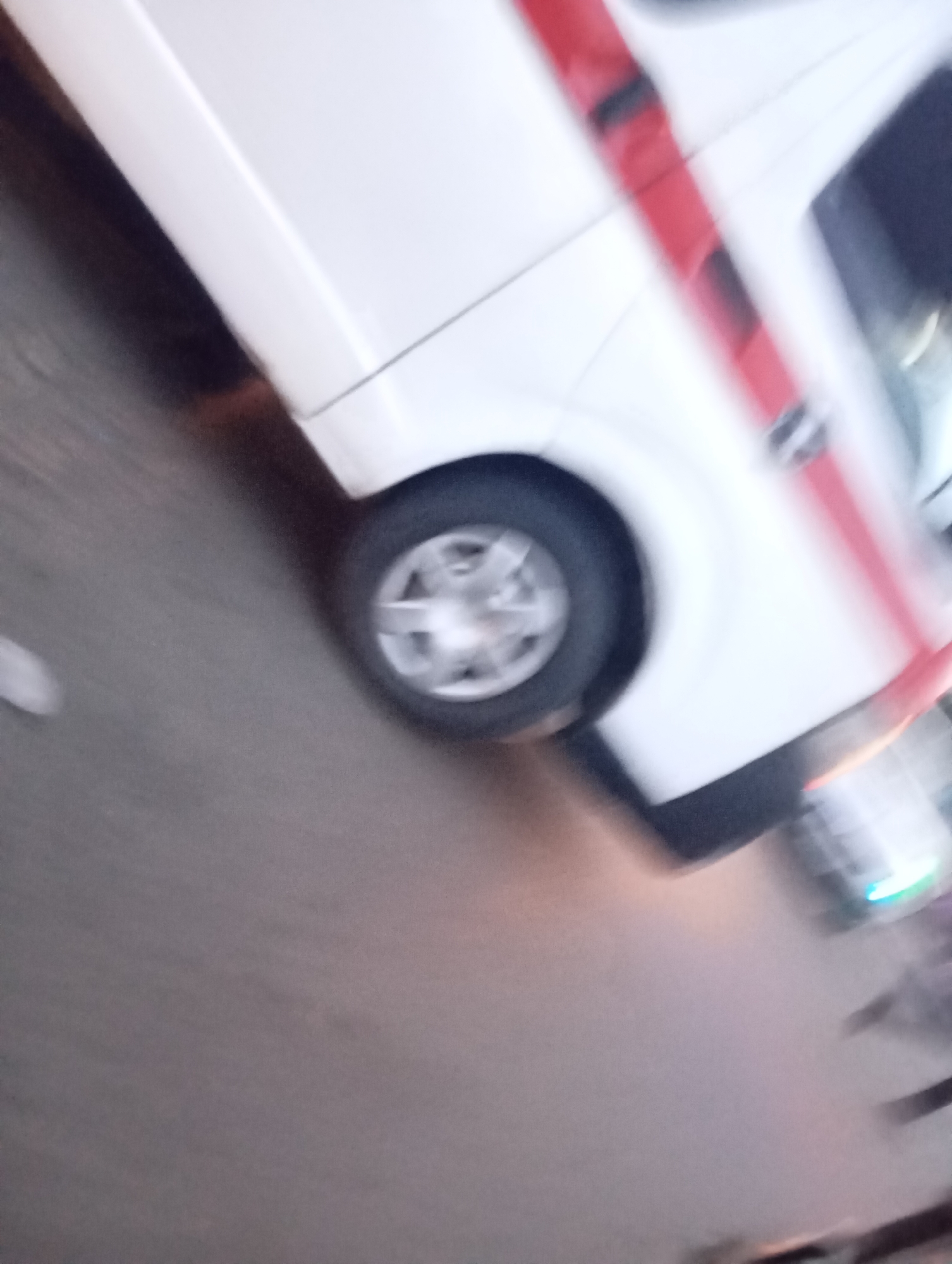 A blurred image shows the side of a white vehicle with a red stripe. The vehicle's wheel is visible, and it appears to be on a road in Port Harcourt, Nigeria. The background is indistinct, suggesting motion or low light conditions.