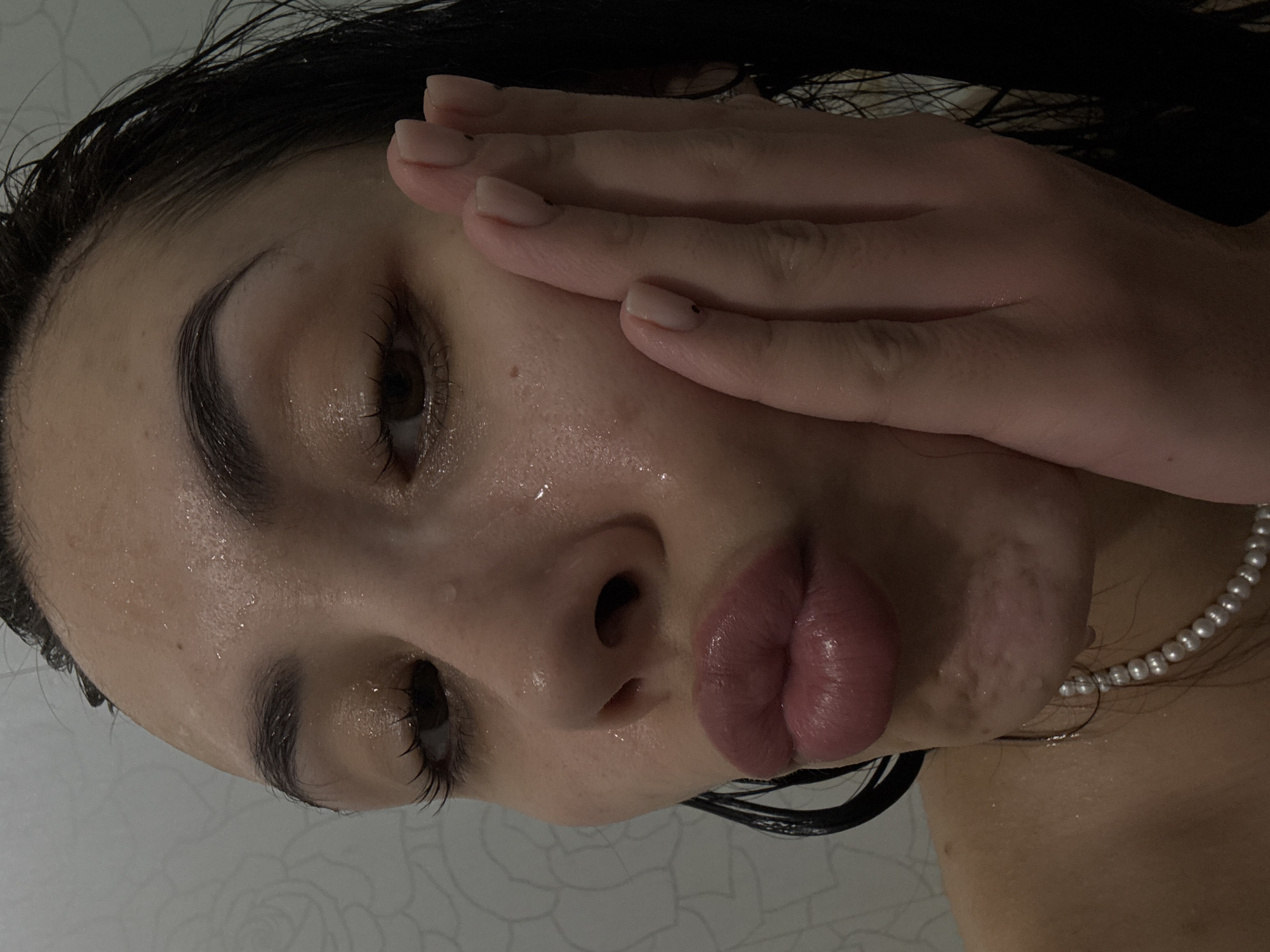 A close-up photograph depicts a woman with dark hair, wet skin, and a pearl necklace. Her face is tilted, and one of her hands is touching her cheek. The location, Votkinsk, Russia, cannot be determined from the visual information provided.