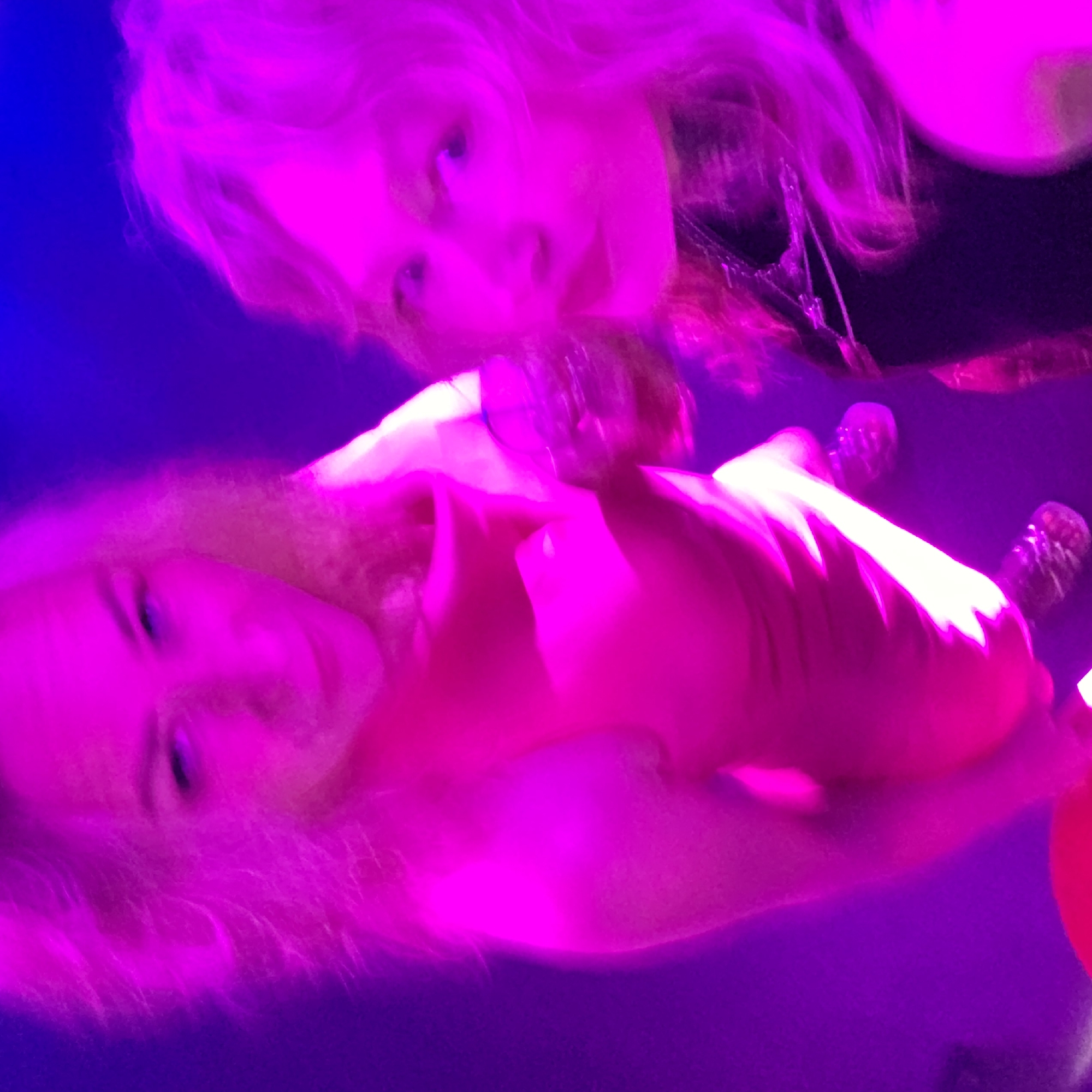 Two people are posing for a picture. They are bathed in pink and blue light. They are likely indoors. The location is unknown.