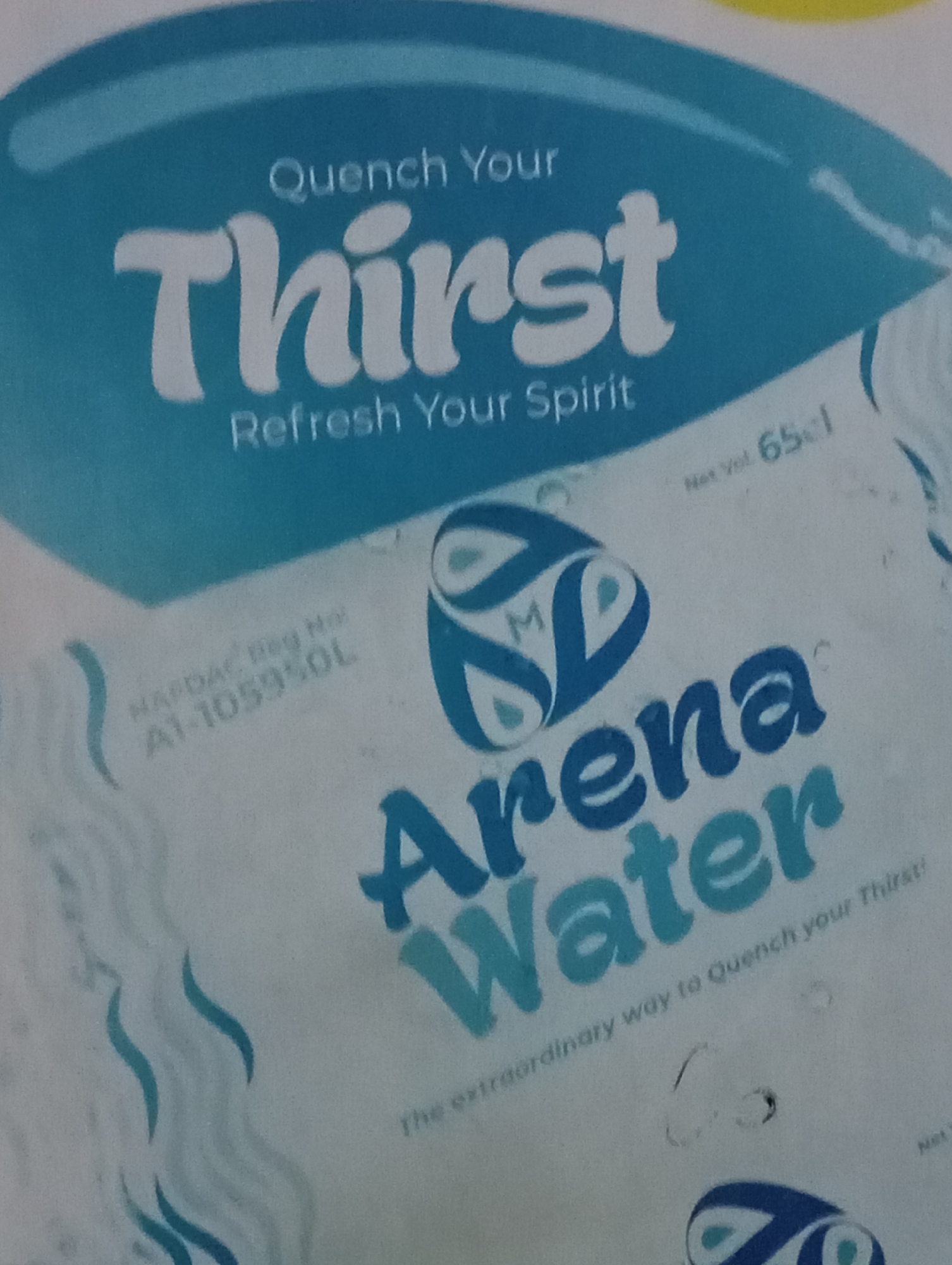This media file is a close-up, slightly blurry, overhead shot of what appears to be packaging for a beverage. The dominant colors are shades of blue and white, with a hint of yellow at the top. The text "Quench Your Thirst" and "Refresh Your Spirit" are prominently displayed in large, stylized white font against a bright blue background. Below this, "Arena Water" is written in a combination of dark blue and teal, with "Arena" in a more elaborate font and "Water" in a simpler, blocky font.
Additional text elements are visible, including "Net Vol 65cl" and "NAFDAC Reg No A1-105950L". A logo featuring intertwined blue shapes and light blue dots is positioned between the "Thirst" and "Arena" text. A wavy, abstract pattern in shades of blue is visible on the left side of the image, suggesting a water-like theme.
The bottom of the image shows the phrase "The extraordinary way to Quench your Thirst!" in a smaller font, curving around the "Arena Water" text. There are also some unclear circular markings and smudges on the packaging. The overall impression is of marketing material for a water product, emphasizing refreshment and thirst-quenching qualities. The lighting is bright, and there are no visible people or specific environmental cues to determine the time of day, weather, or location. The focus is entirely on the product branding.