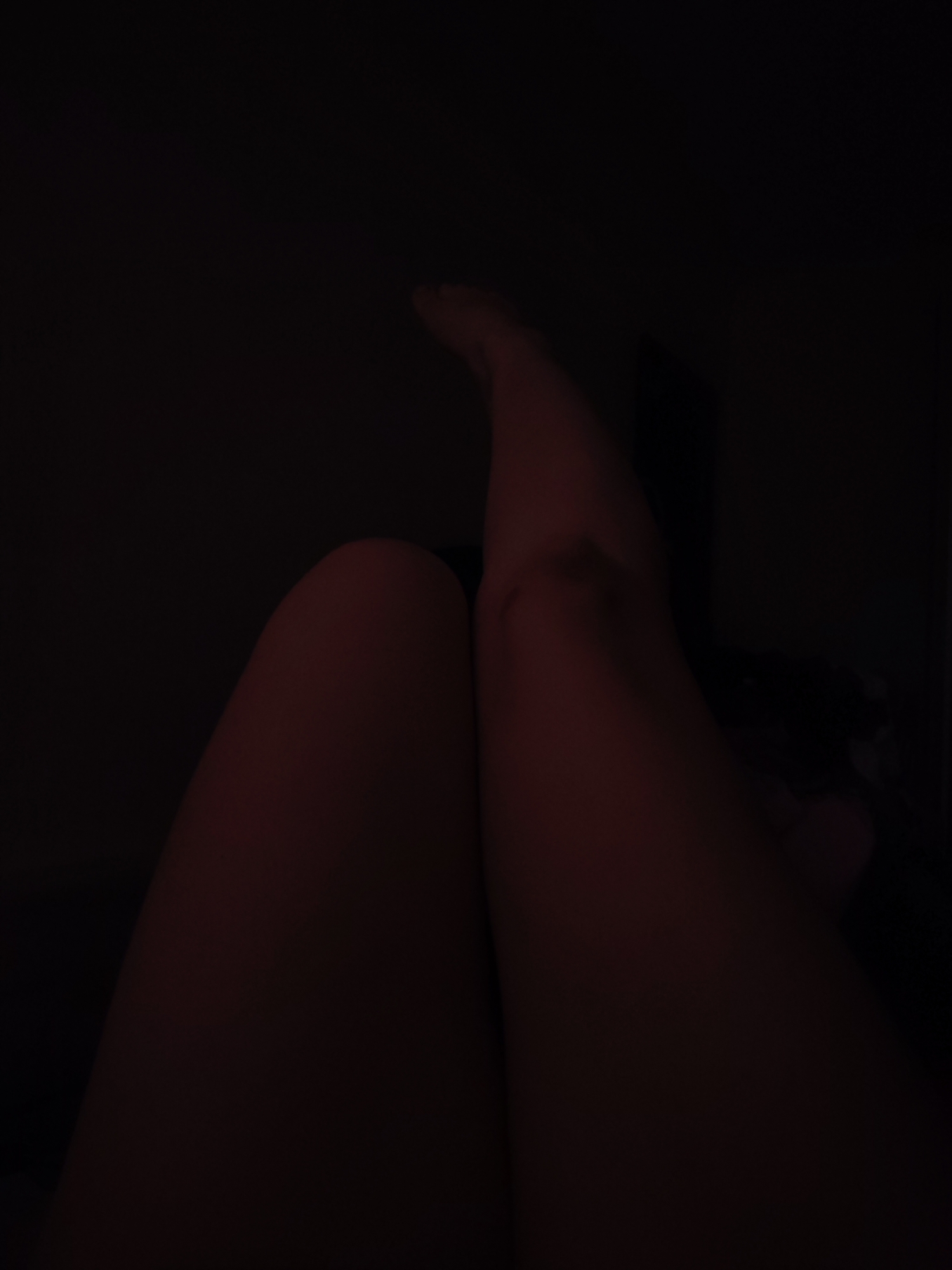 The image shows a close-up view of a person's legs, likely in a dark or dimly lit room. The legs are positioned in the foreground, with one leg crossed over the other. The feet are visible at the top of the image. Due to the darkness and limited details, it is impossible to determine the exact location, including whether it is in Izhevsk, Russia.