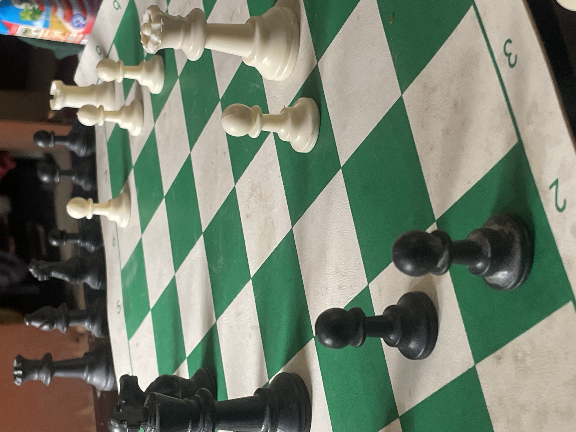 A close-up shot of a chess board with several chess pieces. The board is green and white. White chess pieces include a queen, a rook, and two pawns. Black chess pieces include pawns, rooks, bishops, and a queen. Numbers 2, 3, 5, and 6 are visible along the edge of the board. The location is not discernible from the image. Jos, Nigeria, is not determinable from the image.