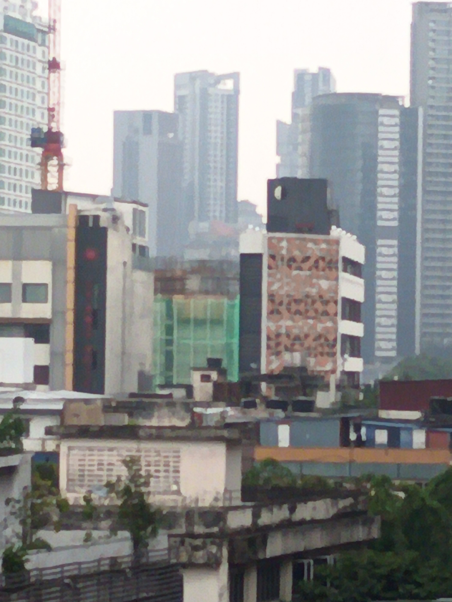 The image depicts an urban landscape with several tall buildings, a construction crane, and a bridge. The buildings vary in architectural style and height, with some featuring intricate patterns on their facades. Green netting is visible on one of the buildings, suggesting ongoing construction or renovation. Several trees are scattered throughout the scene, adding a touch of nature to the urban environment. The sky is overcast, indicating a cloudy day. The scene appears to be a snapshot of a bustling city, likely Kuala Lumpur, Malaysia, given the characteristic mix of modern architecture and ongoing development. The image is a high-angle shot, capturing the vastness of the cityscape.