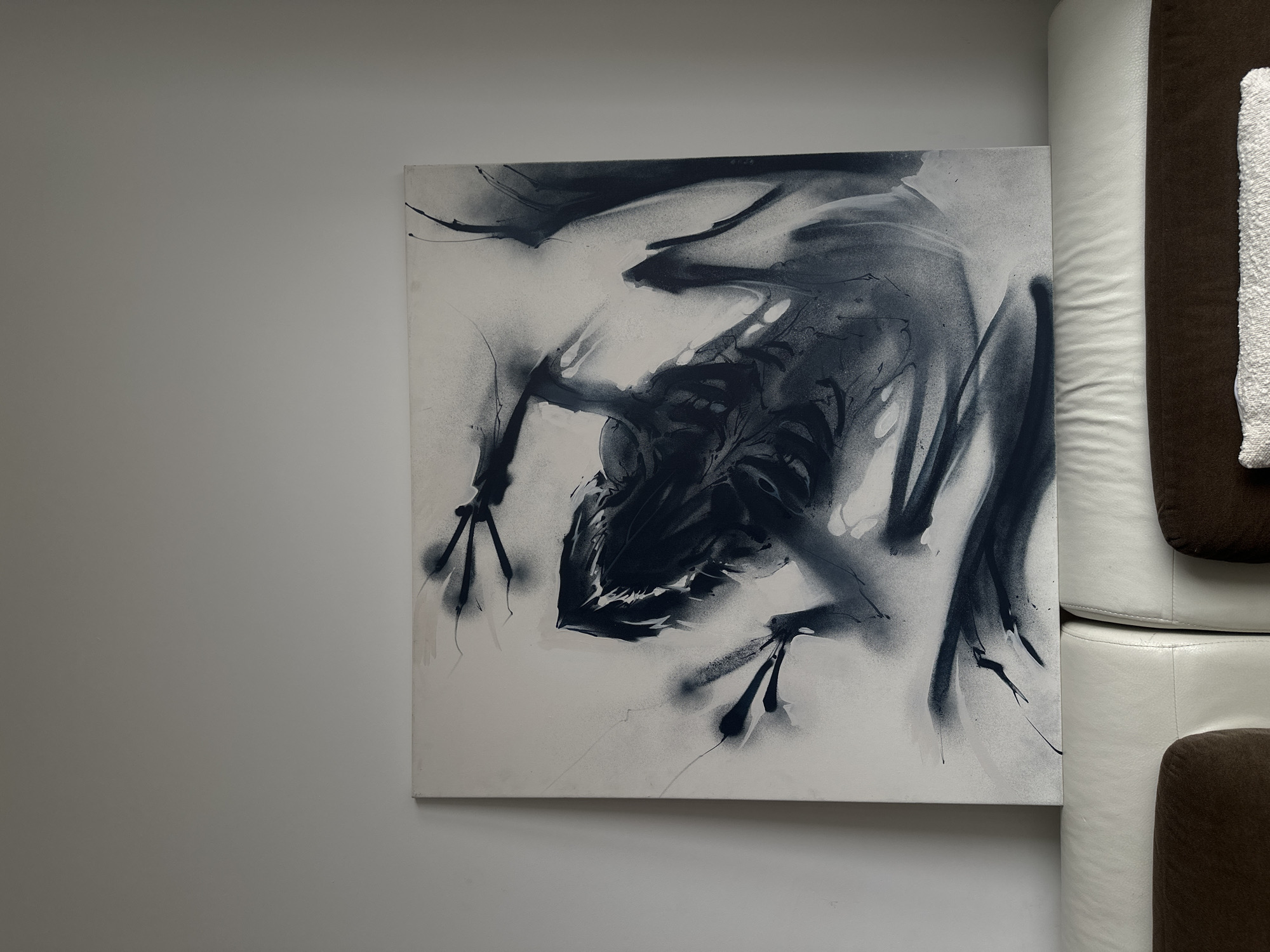 The image shows a painting depicting a creature of indeterminate origin, possibly an abstract representation of a bat or similar winged animal. The artwork uses predominantly black and white tones with a loose, spray-paint style. It is mounted on a wall near a white and brown sofa. There is no information in the image to suggest the location is Khimki, Russia.