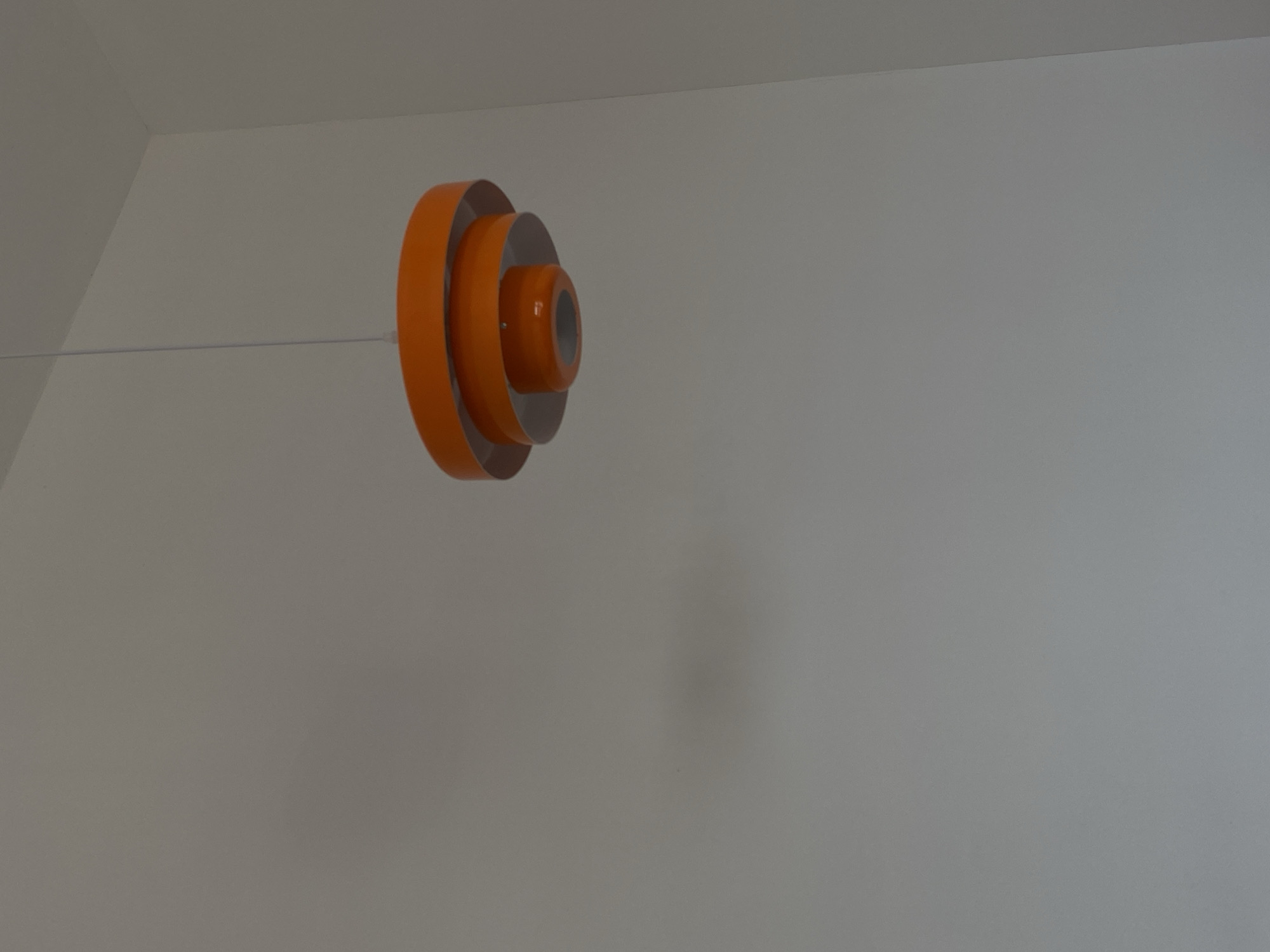 The image shows an orange and silver pendant light fixture hanging in a room. The light is suspended from the ceiling by a thin white cord. The walls are white, and there is a corner visible in the upper left. The location information of Izhevsk, Russia is not discernible from the image.