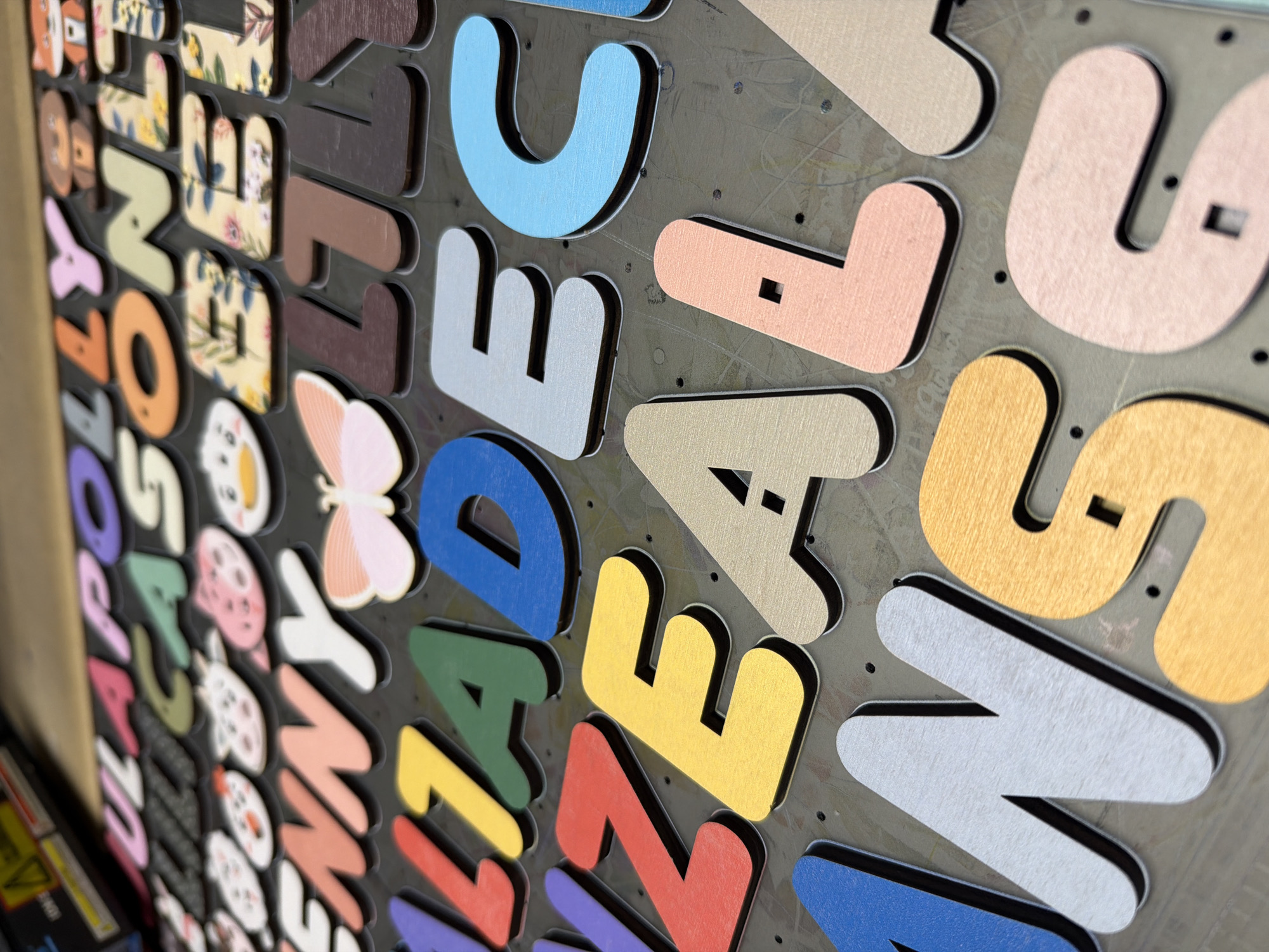 The image shows a collection of colorful wooden letters, some with patterns, laid out on a dark surface. The letters are three-dimensional and appear to be part of a craft or educational material. The surface they are on is textured and has small circular indentations. There are no people or animals visible. The context of Ternopil, Ukraine, is not present in the visual information of the image.