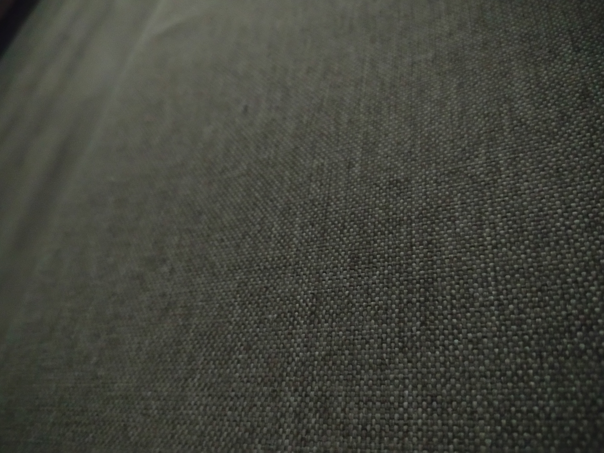 The image shows a close-up of dark grey woven fabric. The weave pattern is visible. The lighting is somewhat dim and uneven. No people, identifiable subjects, or objects beyond the fabric itself are present. No actions or interactions are occurring. There is no indication of the location being Yerevan, Armenia, or any other geographical context.