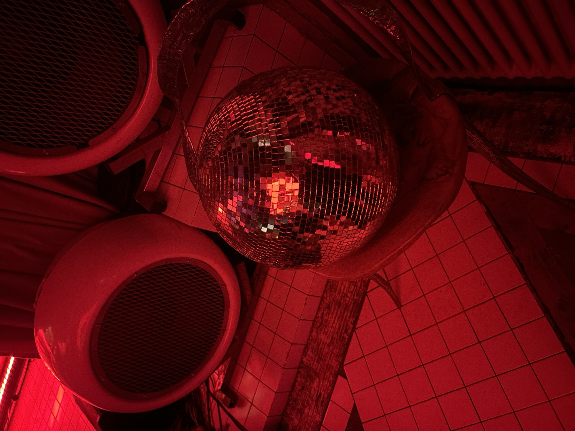 The image shows an interior scene in Moscow, Russia, under a red lighting scheme. A disco ball hangs from the ceiling, reflecting the light in a scattered pattern. Two circular objects with metal mesh covers are visible, possibly ventilation or speaker systems. The floor is tiled with small squares. The scene's environment suggests a nightclub or entertainment venue.