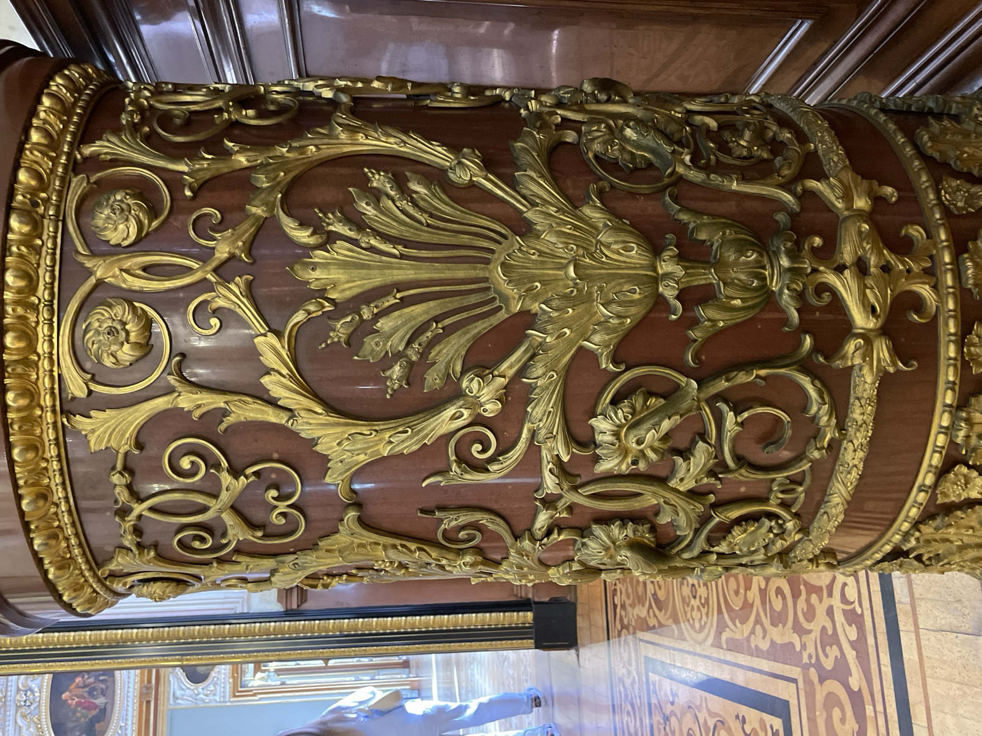 The image shows a section of an ornate, cylindrical object or structure, likely a column or the leg of a piece of furniture. It is richly decorated with gold-colored, three-dimensional floral and foliate designs on a background of reddish-brown wood. The level of detail and craftsmanship suggests it is antique and of high value.
The location is Unknown, Unknown.