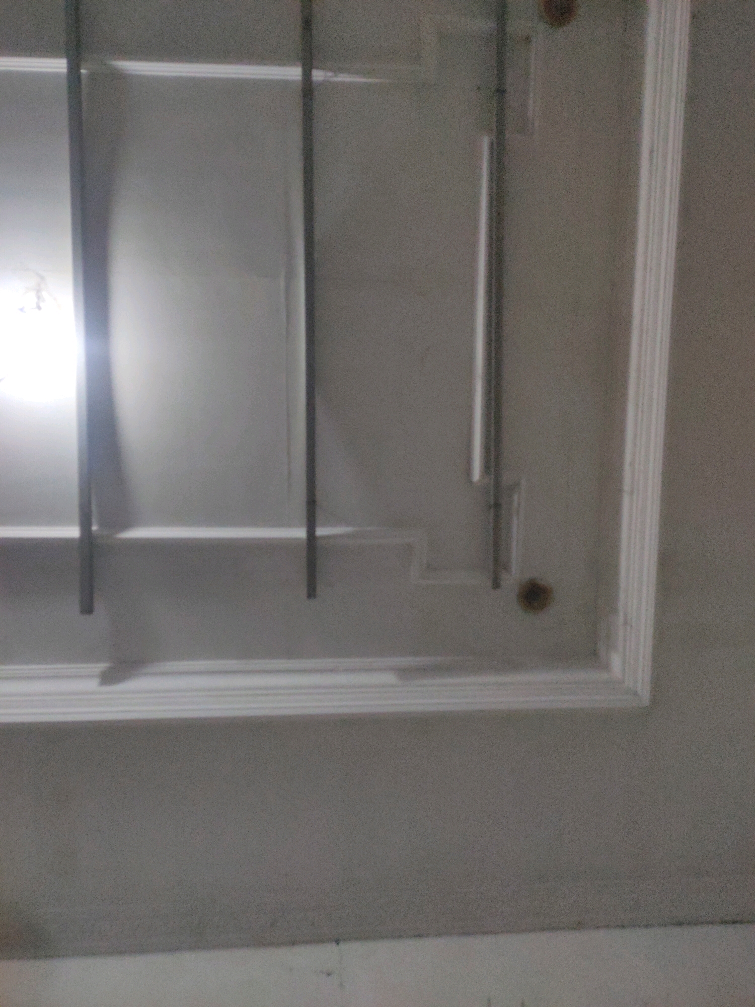 The image shows a ceiling with decorative molding and a light fixture. The molding is white and features multiple layers of detailing. A vertical metal bar extends from the ceiling, and another similar bar is partially visible. A light source creates a bright glare on the left side of the image, reflecting off the ceiling. The overall scene appears to be an indoor environment, possibly a room in a building. There are no people, animals, or vehicles visible in the image. The location is identified as Pulungan, Indonesia.