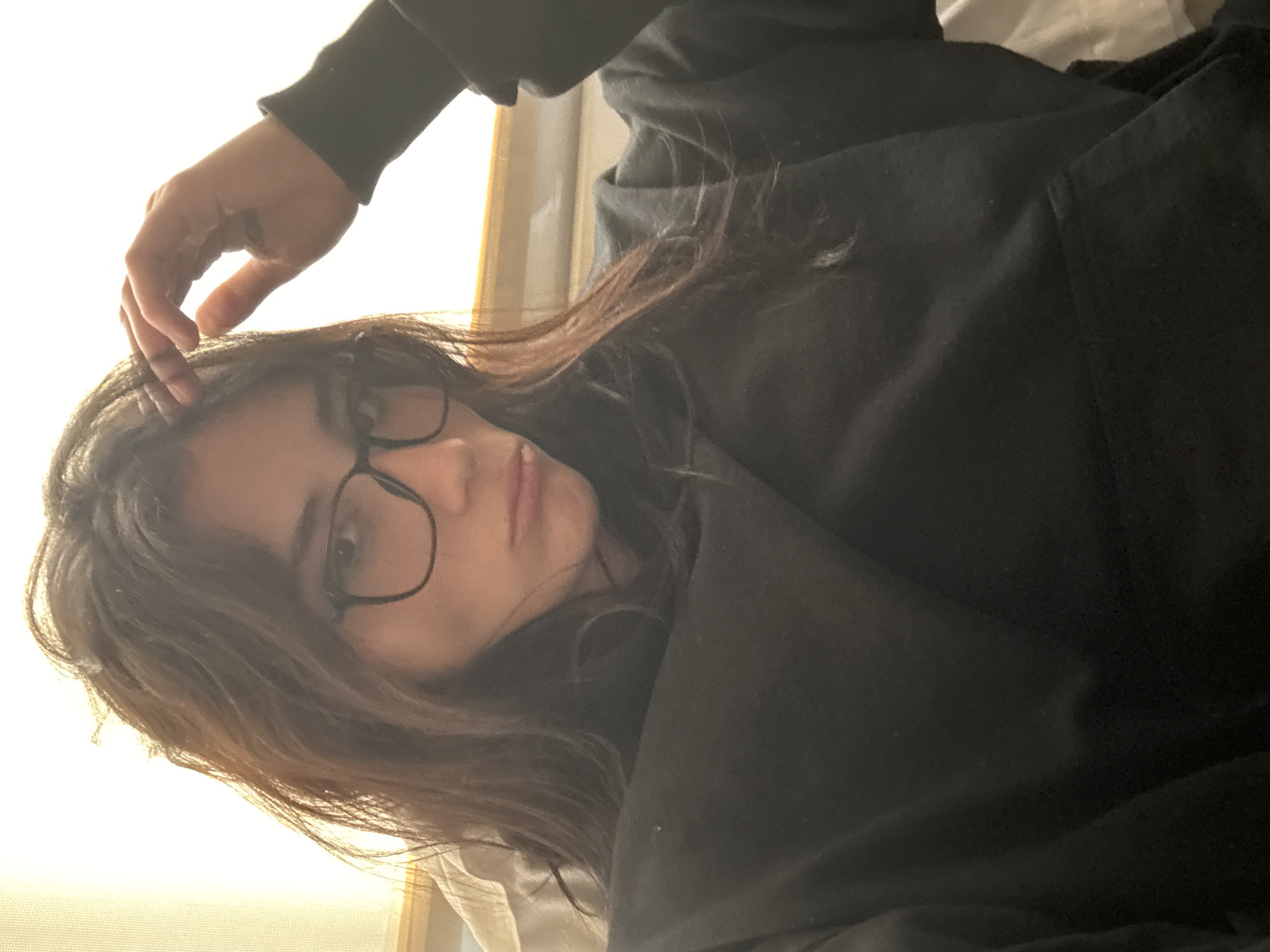 A woman with brown hair and glasses is lying down, possibly on a bed, wearing a black hoodie. Her hand is touching her hair. The location cannot be determined from the image, nor can the city of Buenos Aires, Argentina, be confirmed.