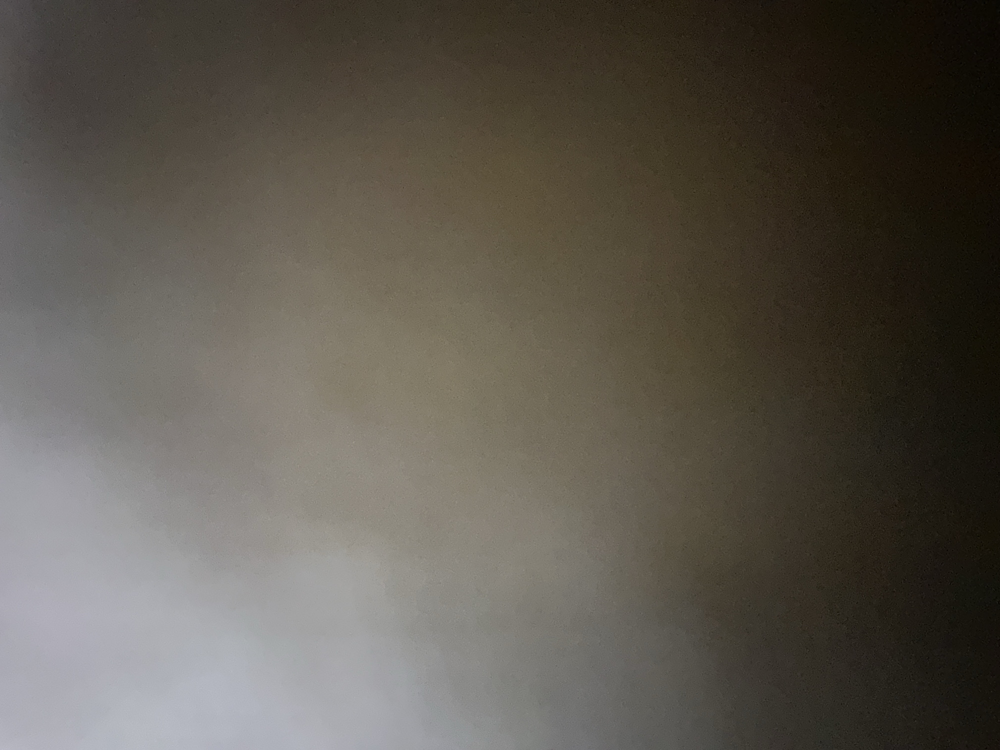 The image displays an abstract gradient of light and shadow, with no discernible subjects, objects, or scene. The top and right portions of the image are dark, transitioning to a lighter, muted gray in the bottom and left. There are no visible signs of activity, events, or any specific details related to time of day, weather, or location. The image is devoid of any text.