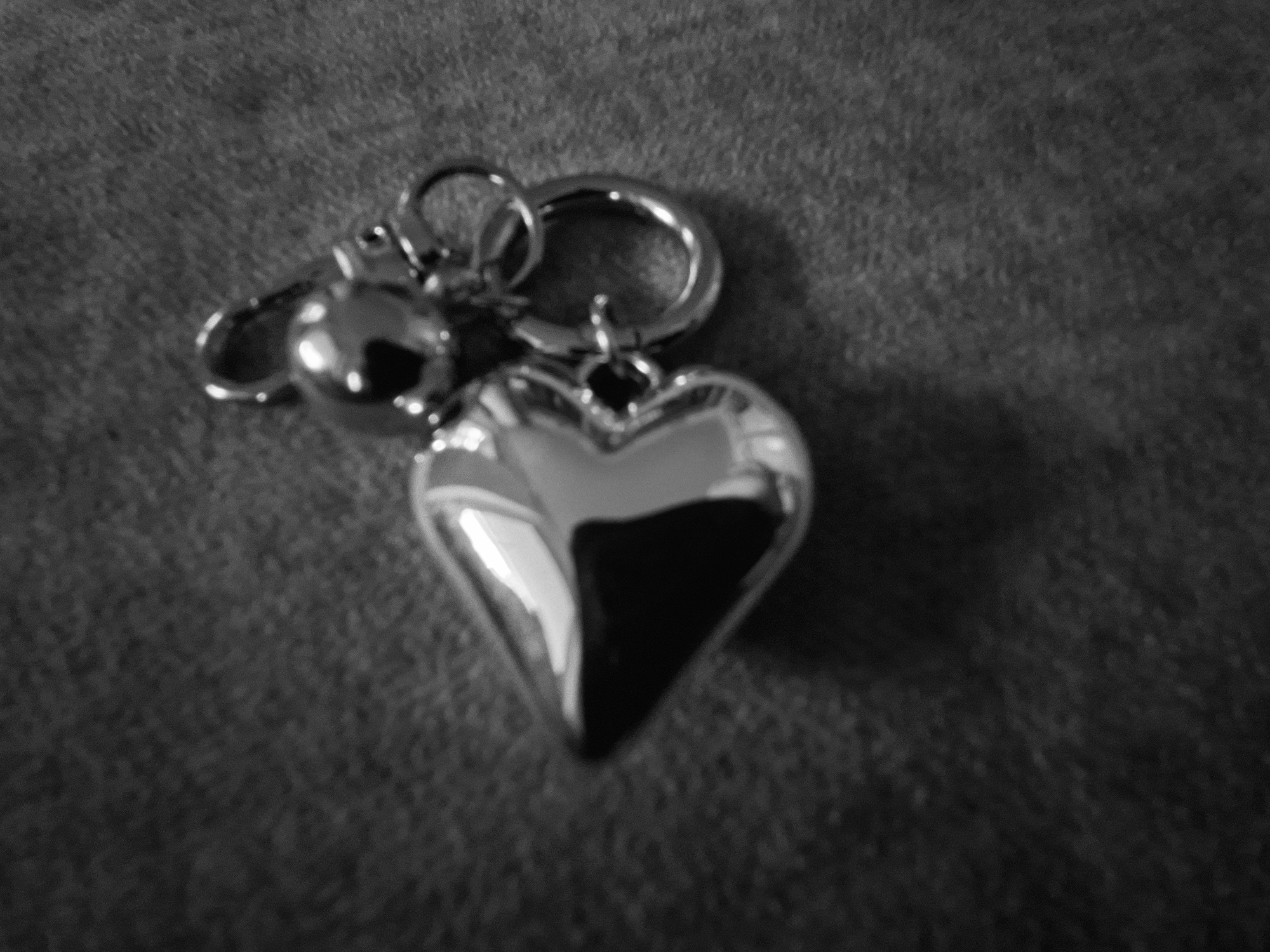 A heart-shaped charm and a round charm are attached to a keyring. The charms are silver and reflect light. The background is a textured dark fabric. The image is a close-up shot, taken from a slightly elevated angle. The overall impression is that of a personal accessory. There is no information that can indicate the location in the city of Baden-Baden, Germany.