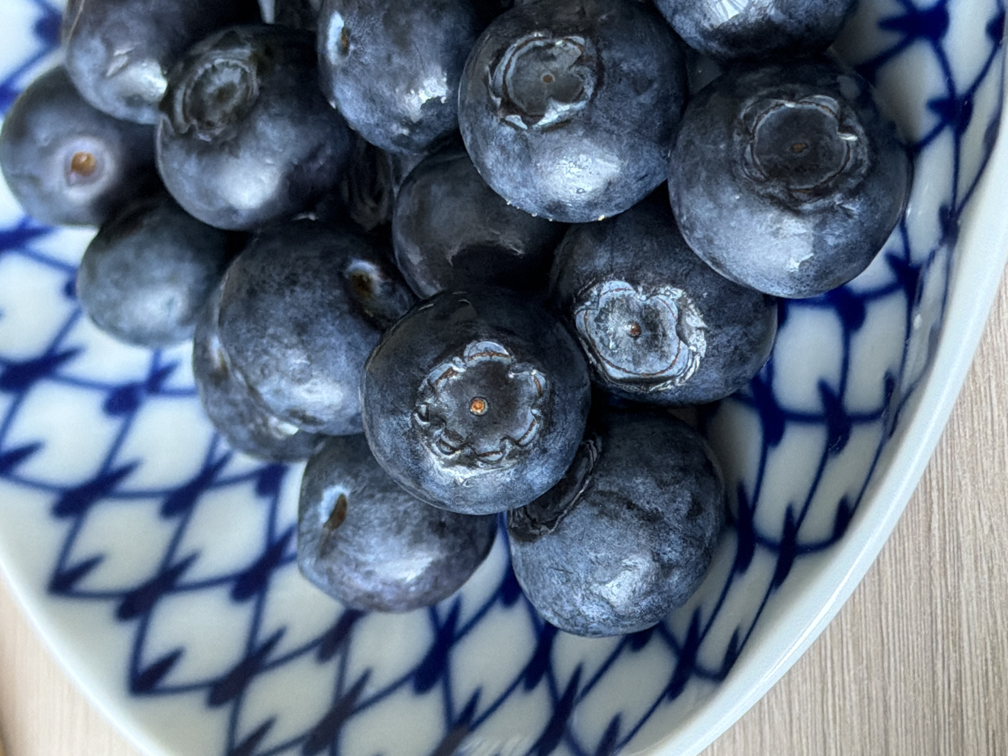 A close-up shot depicts a collection of blueberries nestled in a blue and white patterned dish. The blueberries are dark blue and covered with a light powdery bloom. The dish is resting on a wooden surface. The location and the city of Saint Petersburg, Russia cannot be confirmed from this image alone.