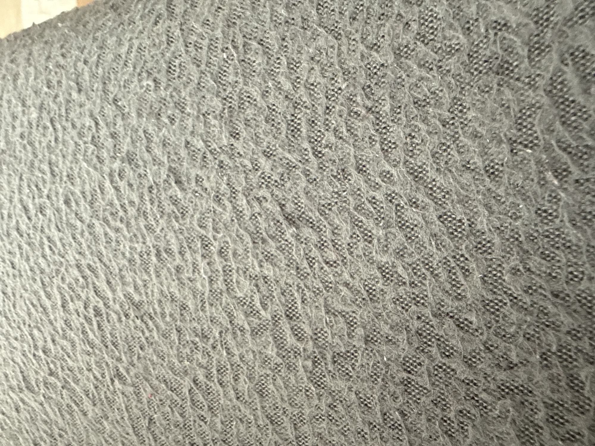 The image shows a close-up of a gray, patterned fabric. The pattern consists of repeating small, diamond-shaped or square clusters of dark material against a lighter gray background. The texture appears soft and possibly knitted. The fabric seems to be covering a surface, possibly a piece of furniture. No people, specific objects or identifiable actions are visible. The context of Lovech, Bulgaria is not apparent within the image.