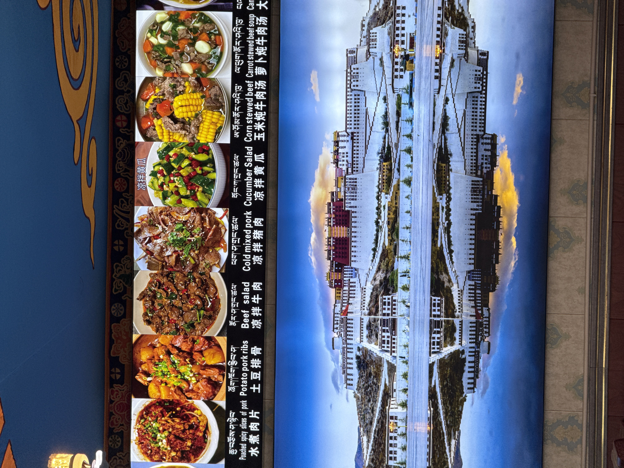 The image displays a menu with Tibetan dishes and an inverted image of the Potala Palace in Lhasa, Tibet, China. The menu items include poached spicy slices of pork, potato pork ribs, beef salad, cold mixed pork, cucumber salad, corn stewed beef, and carrot stewed beef soup. The accompanying text is written in Tibetan, Chinese, and English. The image of the Potala Palace shows its iconic white and red architecture against a blue sky with some clouds. The scene appears to be an informational display at a restaurant.