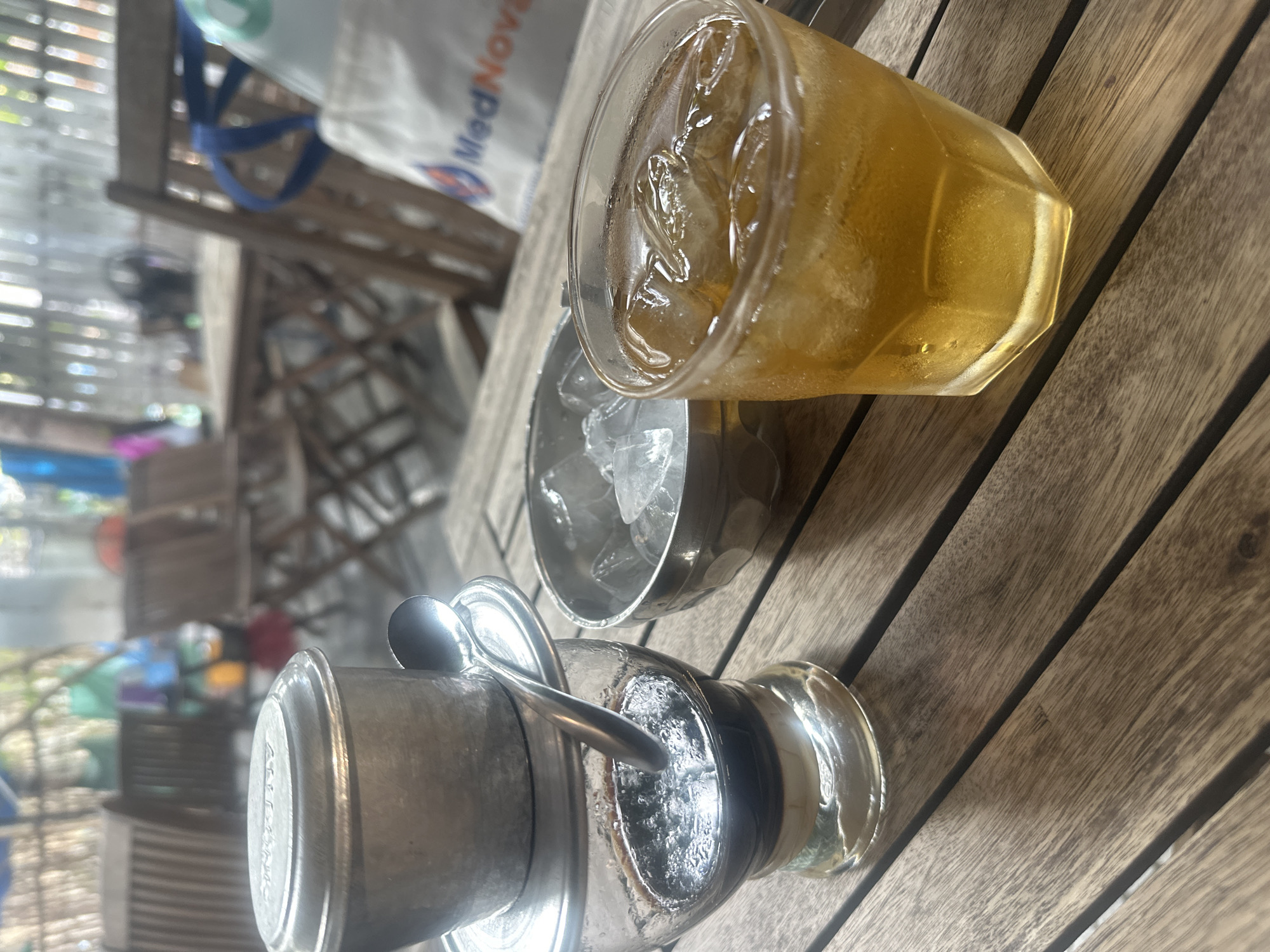 The image depicts a Vietnamese coffee set, consisting of a metal filter on top of a glass, a bowl of ice, and a glass of iced tea. These are placed on a wooden table. The image was likely taken in Nha Trang Ward, Vietnam.