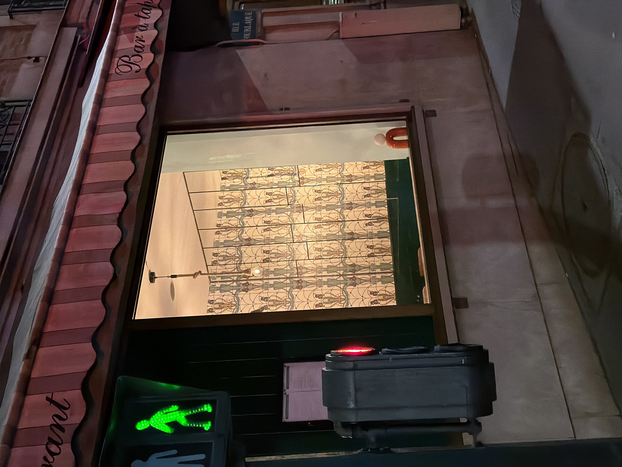 The image shows the storefront of a "Bar à tapas" restaurant located on "Rue Ourlaque" in Paris, France. The storefront has a window with a decorative tiled interior wall visible inside. Outside the restaurant, there is a pedestrian crossing signal with a green "walk" indicator. Also visible is a red light on a device.