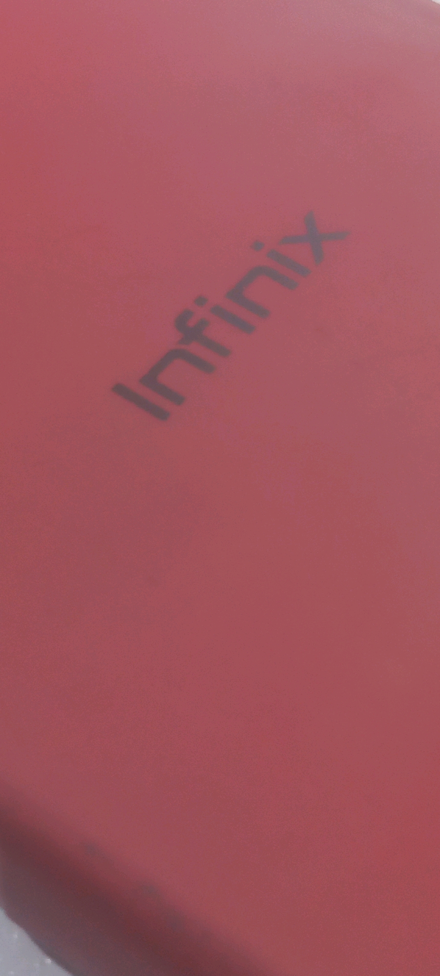 The image shows a close-up, angled view of a red surface with the word "Infinix" embossed in a dark gray, sans-serif font. The text is oriented diagonally from the bottom left to the top right. The lighting creates subtle shadows, giving the letters a slightly raised appearance. The background is a uniform, matte red. There are no people or other identifiable objects in the frame. The location in Rimhala, Lebanon, is not discernible from the image itself.