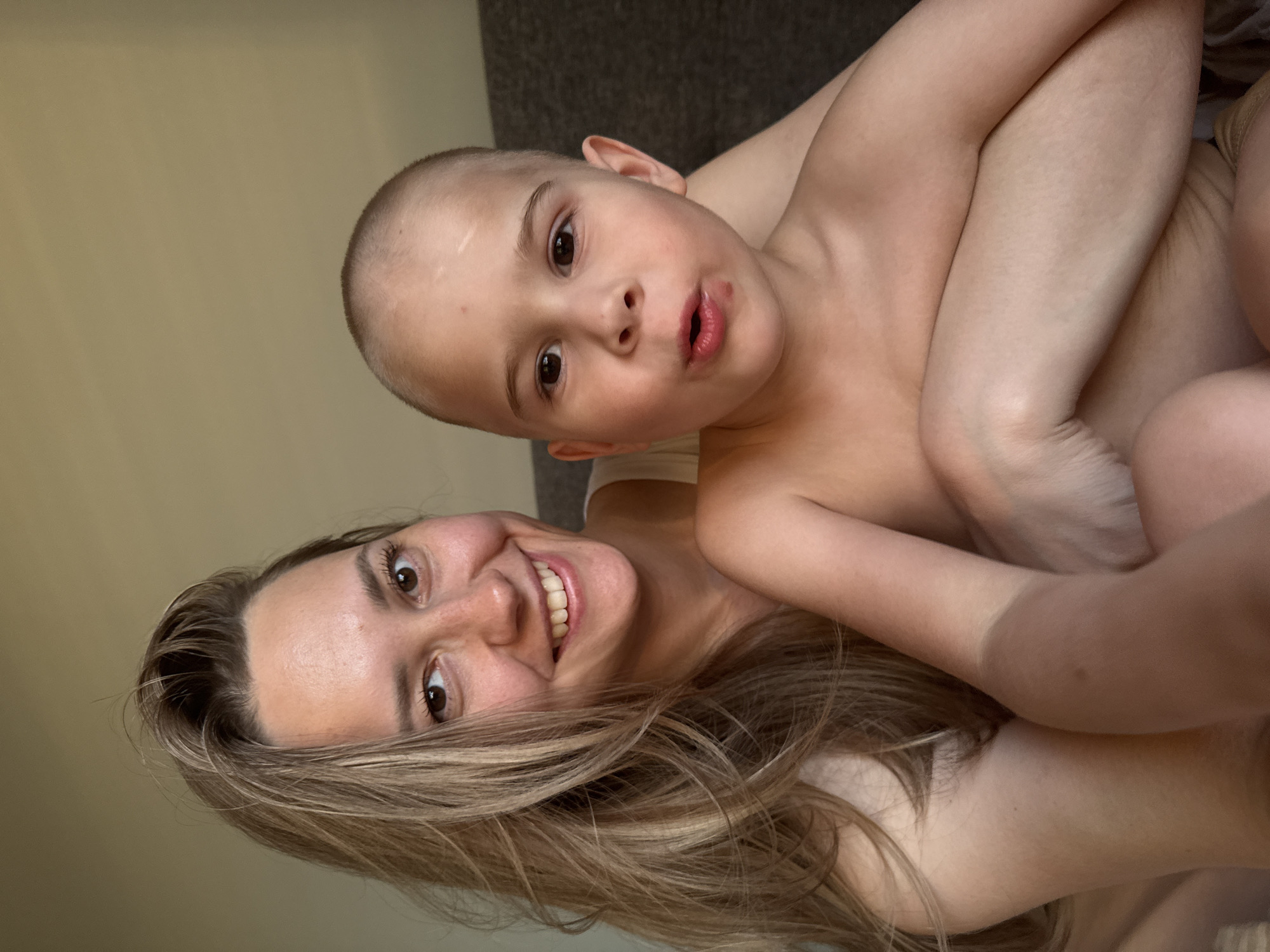 A woman and a young child are in close proximity to each other, possibly embracing. The woman has long brown hair and is smiling. The child, who appears to be male, is fair-skinned and has a shaved head. The background suggests an indoor setting. There is no information to suggest the location is the city of Chaikovsky, Russia.
