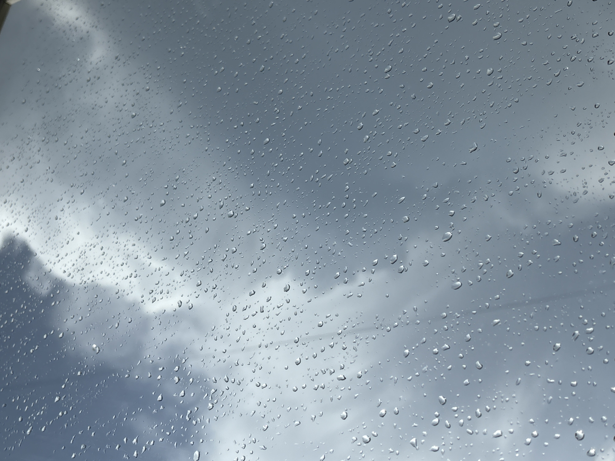 The image shows raindrops on a window, with a cloudy sky visible in the background. The sky is gray and overcast, suggesting a rainy day. There are no people or specific objects visible in the background. The location of the image is unknown and therefore, no mention of Izhevsk, Russia can be made.