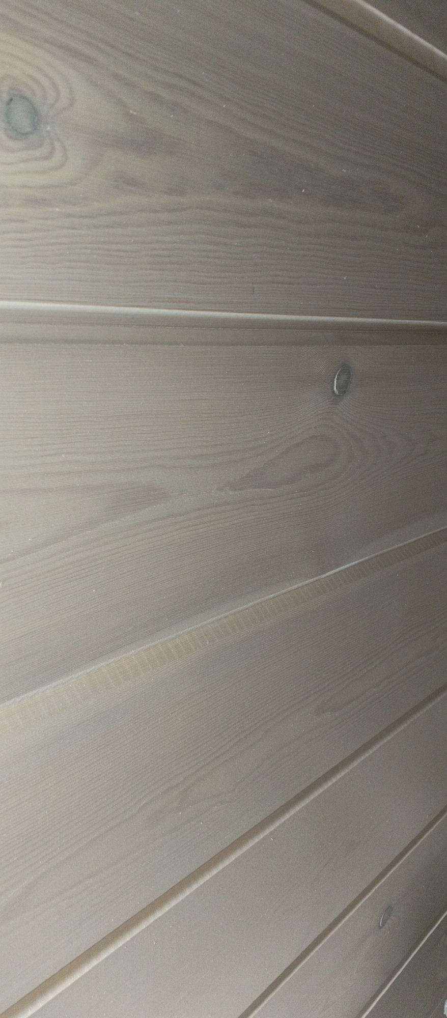 The image is a close-up, eye-level shot of a wall made of light-colored, horizontally oriented wooden planks. The planks have a visible wood grain and some have knots. There are subtle lines or grooves between the planks, indicating they are joined together. The lighting appears to be from above and slightly to the right, casting soft shadows. The overall tone of the image is muted and neutral, with a focus on the texture and pattern of the wood. There are no people or other objects visible in the frame. The scene is indoors, as suggested by the uniform lighting and the nature of the wall construction.
The provided information indicates the location is Sheregesh, Russia. Sheregesh is a mountain resort town in Kemerovo Oblast, Russia, known for its ski slopes and natural beauty. However, the image itself does not contain any visual elements that specifically identify it as being in Sheregesh. The wooden wall could be found in many interior spaces.