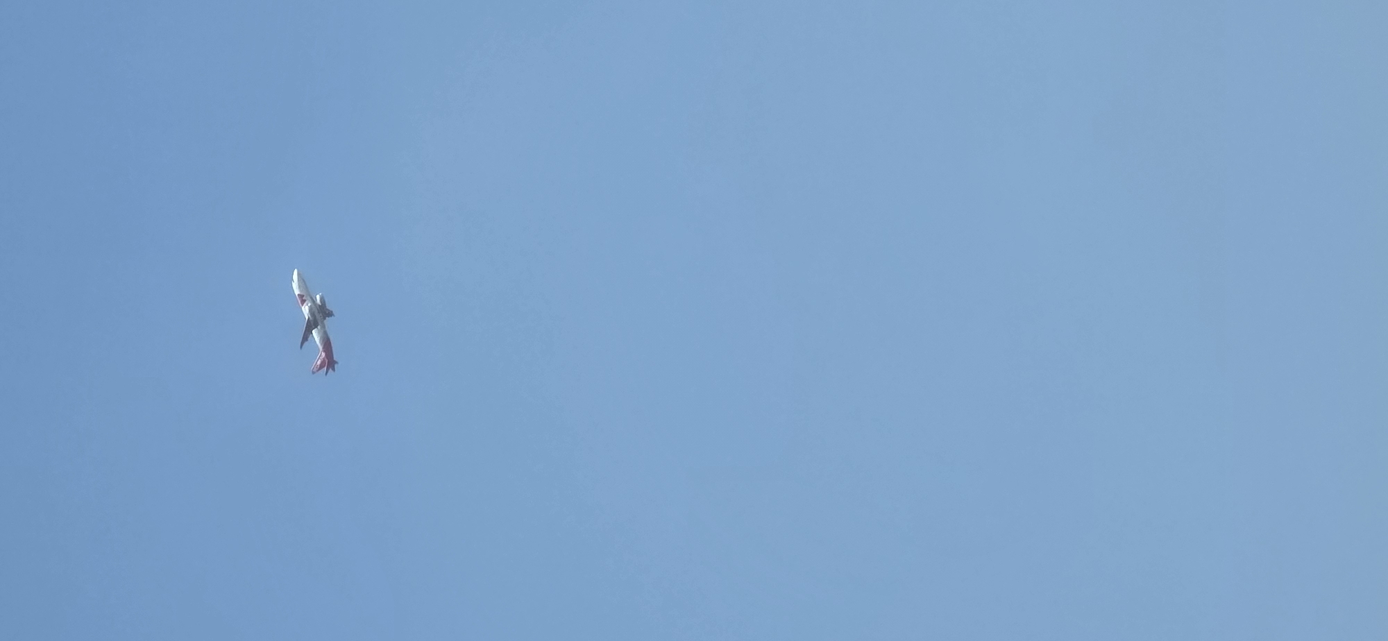 A single airplane is visible in the sky. The plane is white with red accents and appears to be in mid-flight, possibly during ascent or descent, with its landing gear extended. The sky is a clear, uniform light blue, with no clouds or other atmospheric phenomena visible. The image does not contain any information that would allow for localization to the city of Mineralnye Vody, Russia, or any other specific geographical location. There are no people, buildings, or ground features present in the image.