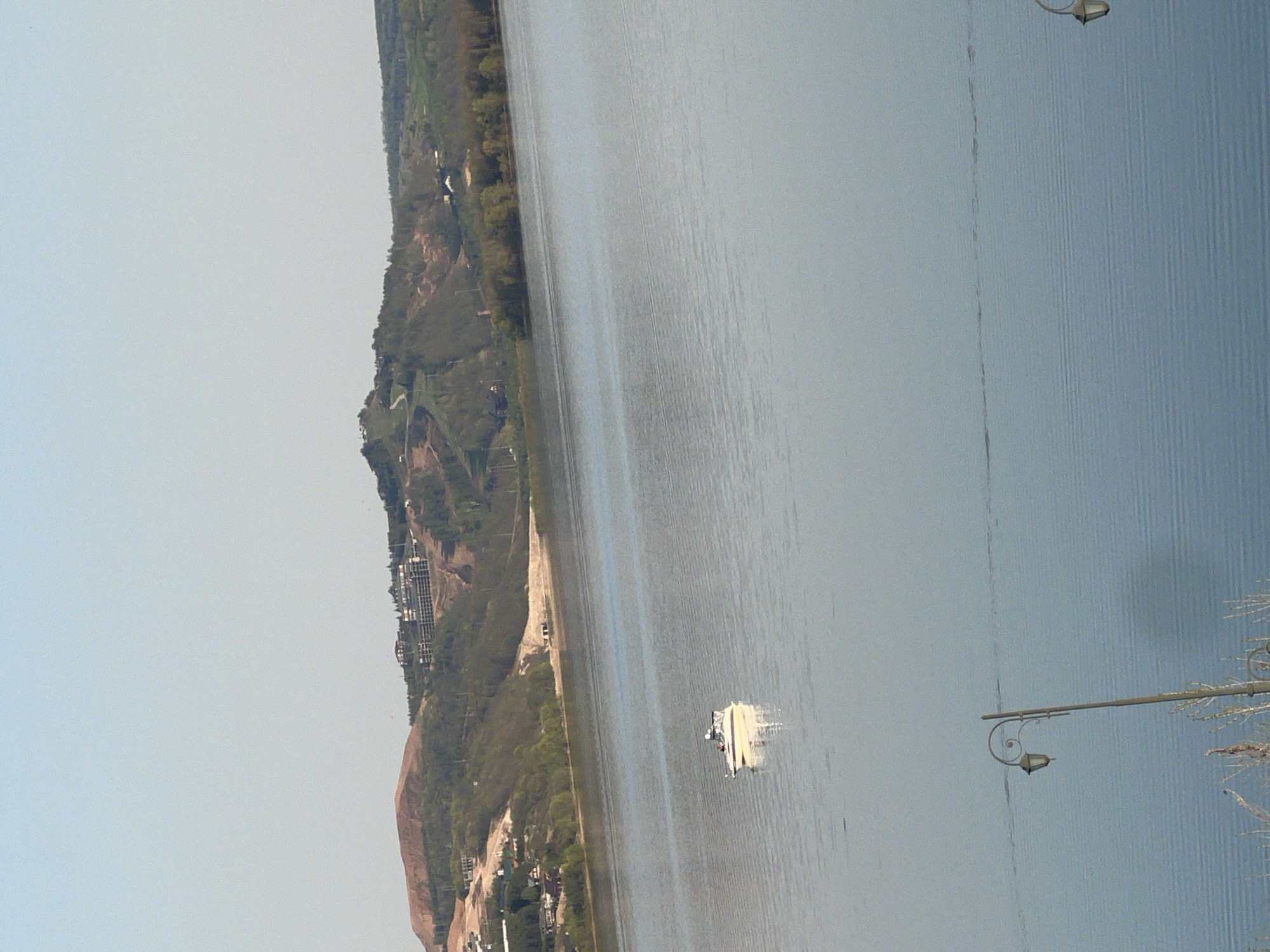 The image depicts a view of the Volga River in Sviyazhsk, Russia, with a shoreline featuring vegetation and buildings. A boat is visible on the water. There are streetlights on the bank. The sky is overcast.