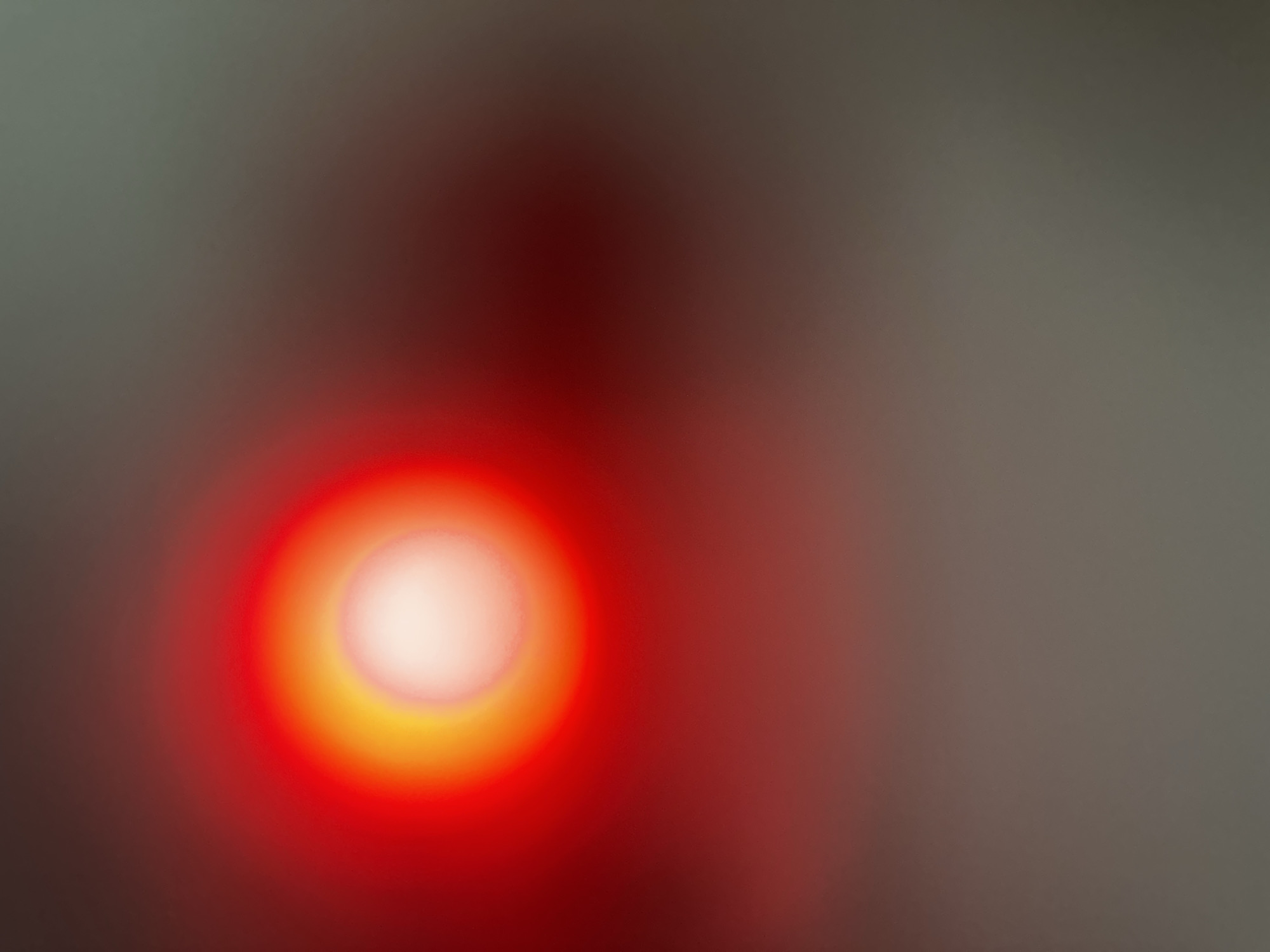 The media file is an abstract, blurred image dominated by a bright red and yellow circular light source. This light source appears to be in the lower left quadrant of the frame and is surrounded by softer, diffused red and gray hues. The background is a gradient of grays, transitioning to darker tones on the left and lighter tones on the right. There is a faint suggestion of a human-like shadow or form behind and above the bright light, which is heavily blurred and indistinct.
The image lacks specific details about time of day, weather, or explicit location cues, beyond the provided context of Belgrade, Serbia. No text is visible. The overall impression is one of an abstract representation of light, possibly from a LED or a similar artificial light source, with a hint of a shadowy presence. The activity or event is not discernible due to the abstract and blurred nature of the image.