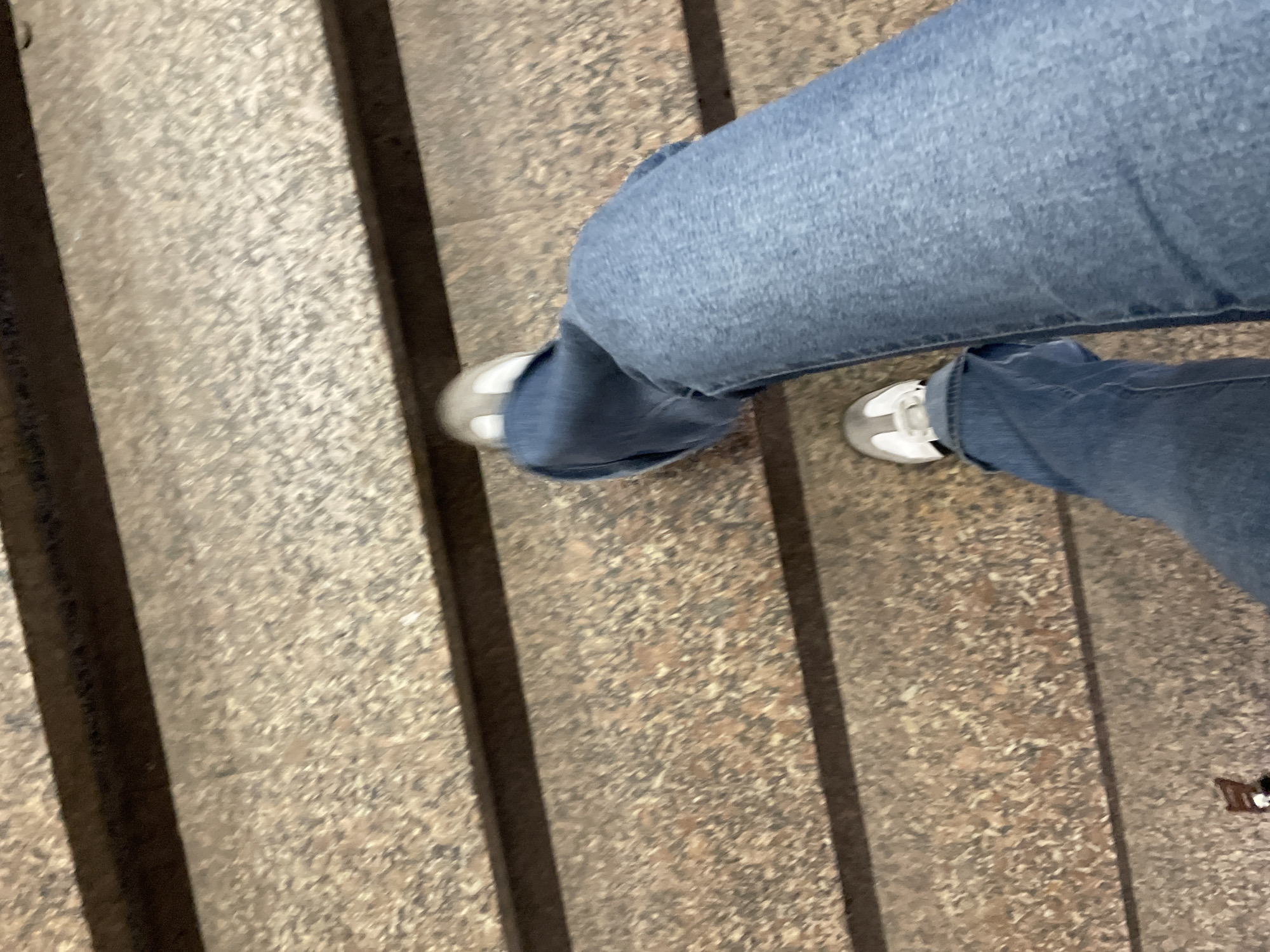 A person wearing blue jeans and gray/white sneakers stands on a staircase. The location is not identifiable as Moscow, Russia. The environment consists of the stairs with linear designs on each step. There are no visible interactions or actions depicted other than standing.