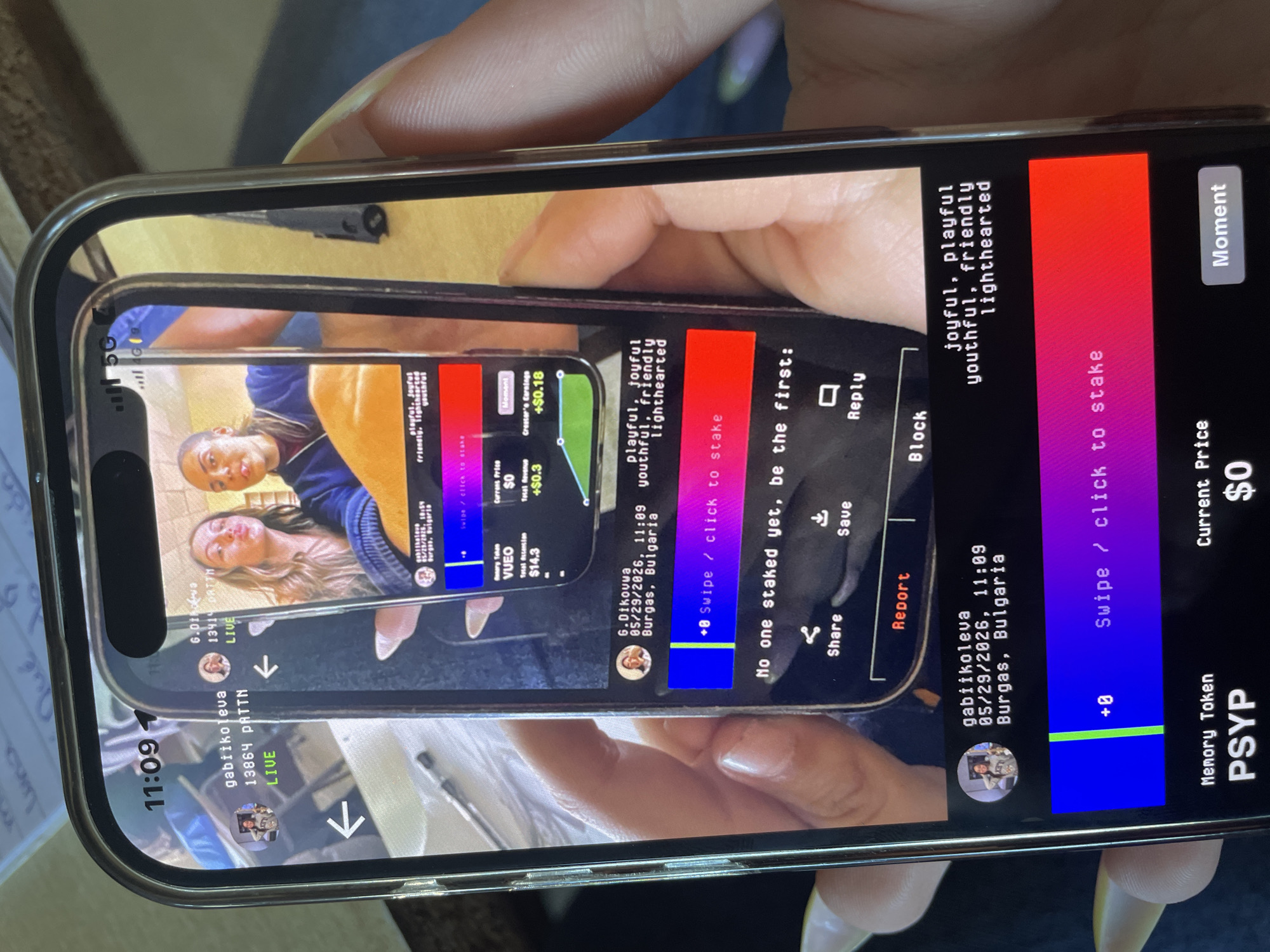 The image shows a person holding a smartphone displaying another smartphone screen, creating a recursive effect. The smartphone being displayed appears to be running an application with live-streaming content. The username "gabiikoleva" is visible in the stream, along with another user identified as "6.Dikowwa" who is listed as being in Burgas, Bulgaria. The app's interface also shows monetary values like "Total Revenue" (+$0.3), "Total Attention" ($14.3), and "Creator's Earnings" (+$0.18). The timestamp on one instance of the screen is 05/29/2026, 11:09. The app seems to involve staking and a "Memory Token" called PSYP.