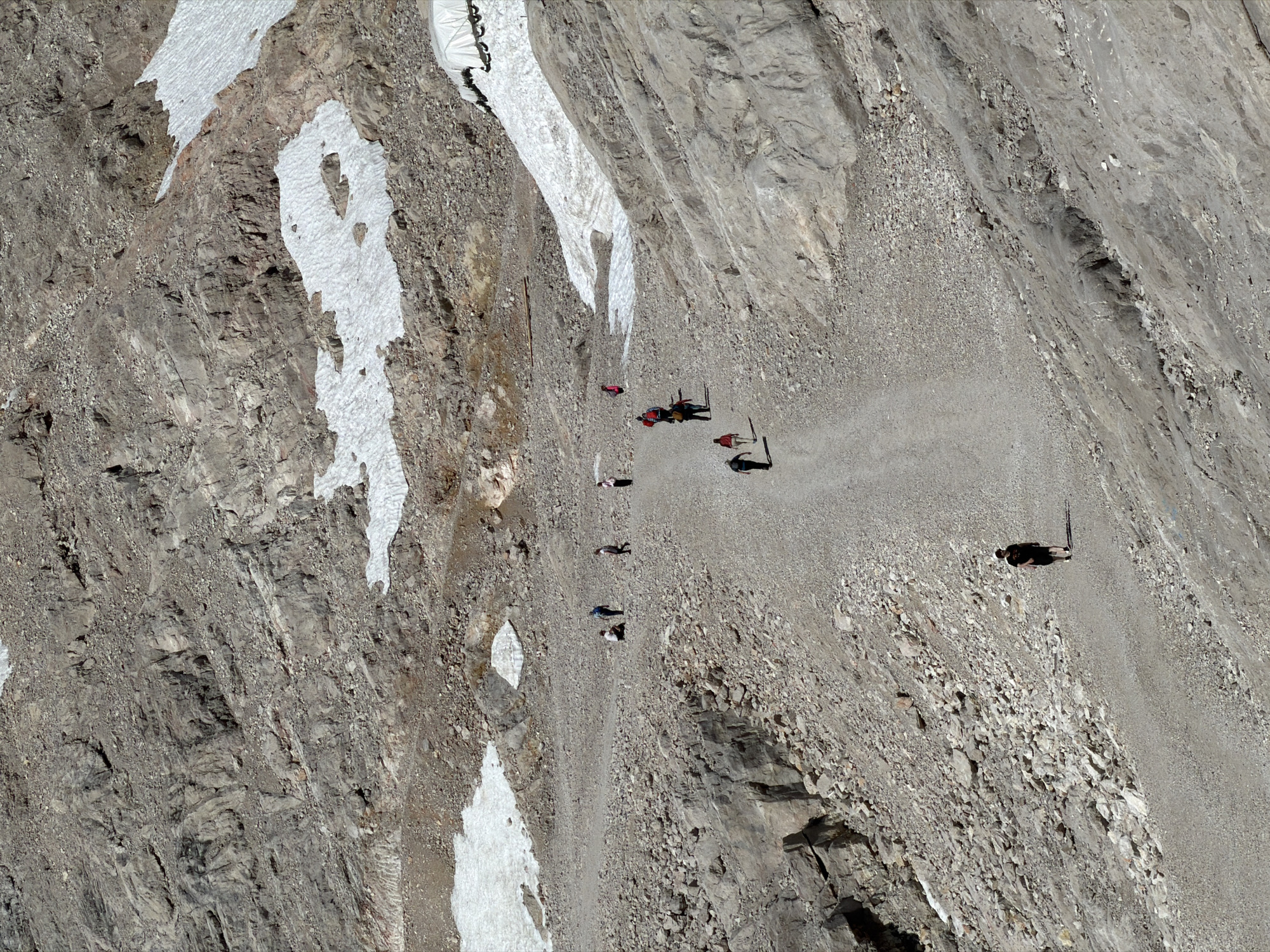The image depicts a mountainous, rocky terrain with patches of snow. Several individuals are visible walking on a gravel path that winds through the landscape. The environment appears to be a popular hiking or climbing area, given the presence of a well-worn path and the casual attire of the individuals. The area suggests a high altitude location, likely a mountain resort or natural park. Without further information, it's impossible to specify the exact location within Garmisch-Partenkirchen, but it is characteristic of the alpine environment found in the region.