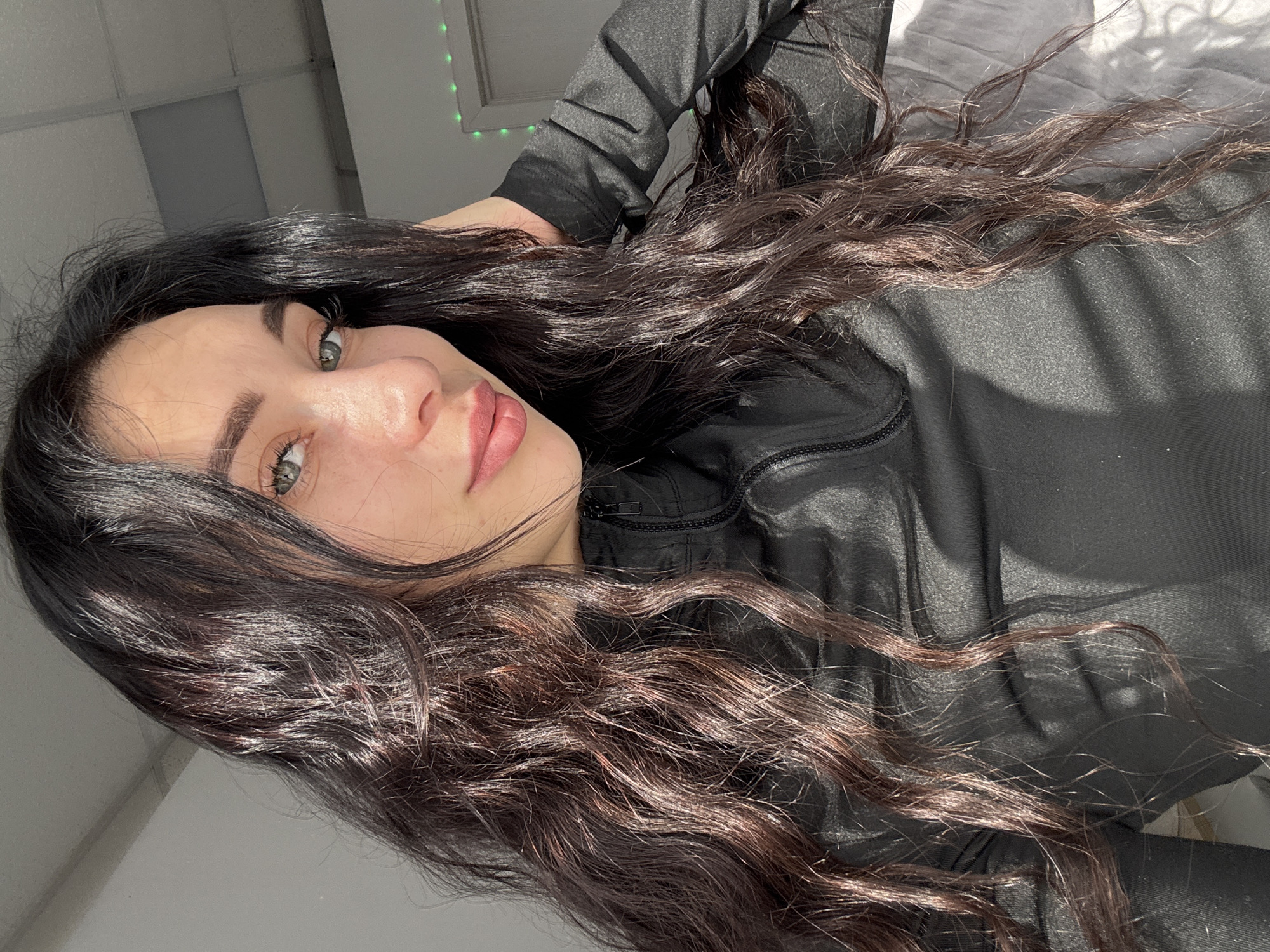 A young woman with dark, wavy hair is lying on a bed. She is wearing a black jacket. The background shows a ceiling with a window or light fixture. The location Фоки, Russia is not identifiable within the image.
