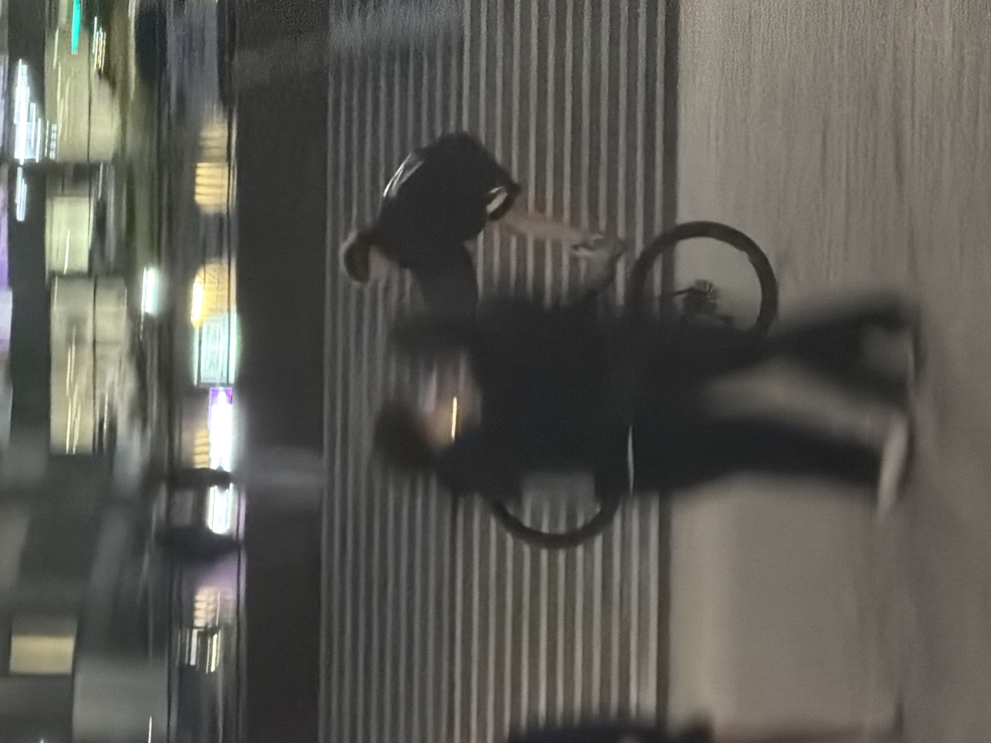 A cyclist is riding on a city street, a building with illuminated windows is on the left. The building on the right has a vertical line pattern.
