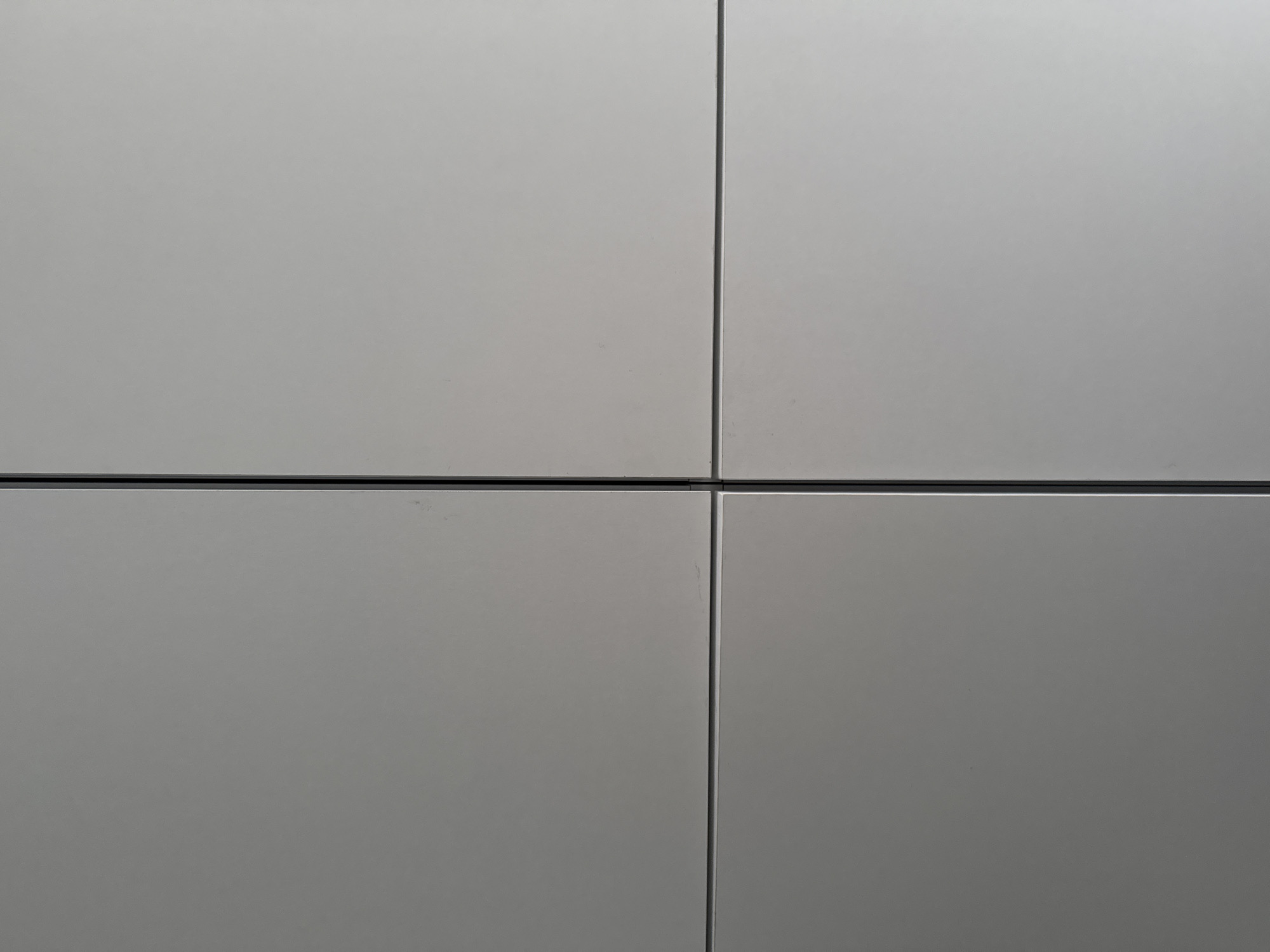 The image shows a close-up of four grey, square panels arranged in a grid. The panels are separated by thin, dark lines. The environment is not discernible from the image.