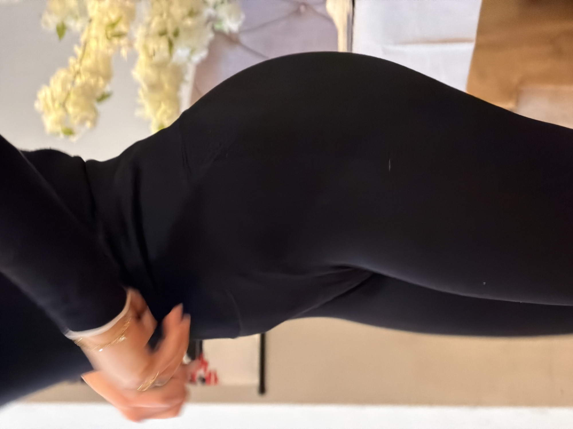 Here is a description of the image:
The image shows a person wearing black leggings. The person's hands are visible, adorned with a bracelet and ring. The background includes a floral arrangement and what appears to be furniture. There is no indication of a location in Sofia, Bulgaria.