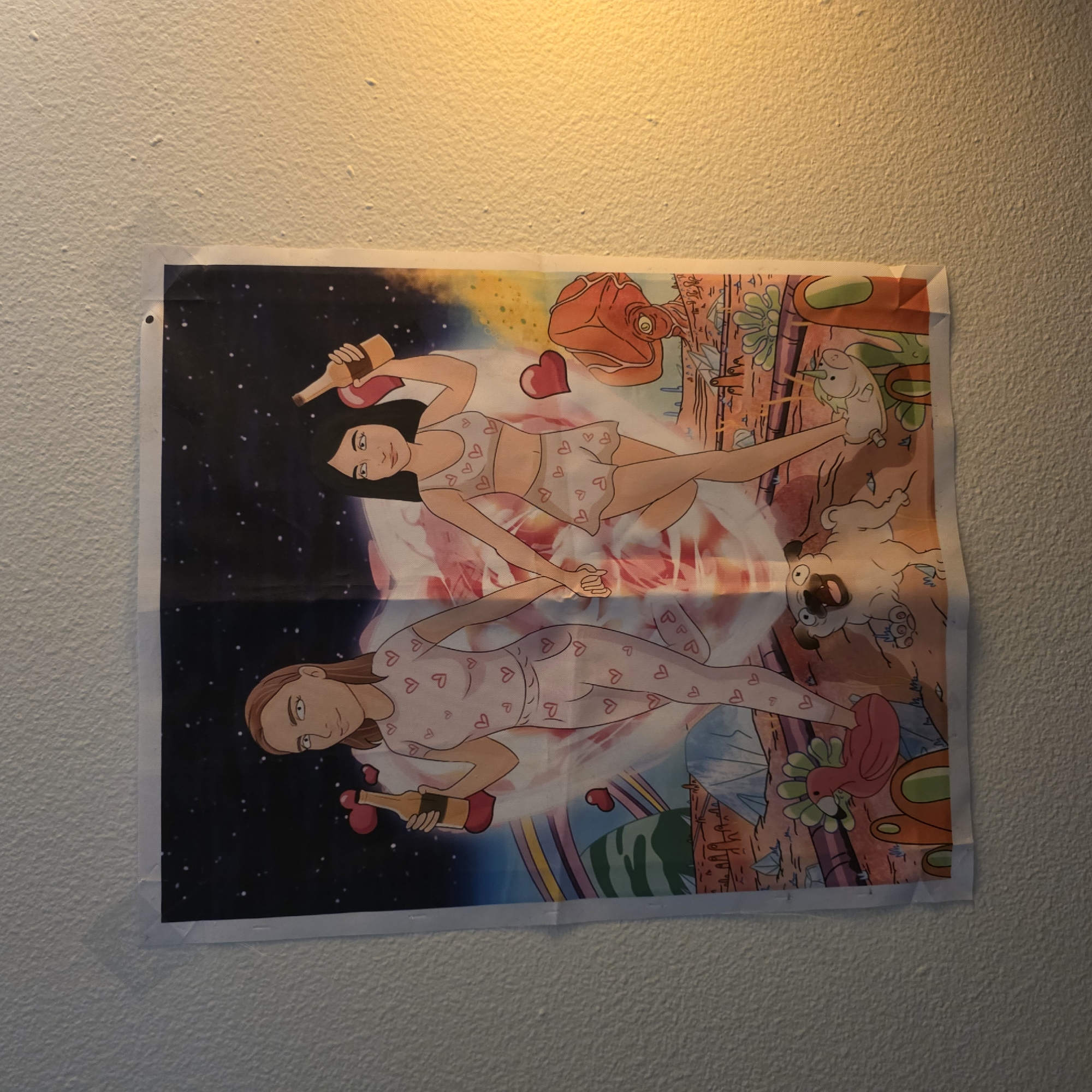 A full-frame, eye-level, wide shot shows a poster hanging on a textured wall, lit by artificial light from the right side. The poster is divided down the center into two halves. The left half depicts a starry night sky with a large pink planet and a rainbow. The right half shows a reddish-orange, desert-like landscape.
On the poster, two cartoon women are depicted holding hands and walking. The woman on the left has brown hair and wears a pink pajama set adorned with hearts. She holds a bottle in her right hand. The woman on the right has black hair and wears a matching pink pajama set consisting of a crop top and a skirt, also decorated with hearts. She holds a bottle in her left hand.
In the foreground of the poster, various cartoon elements are visible. On the left, a pink bird-like creature with green feathers is seen. In the center, a pug dog with its mouth open is looking forward. On the right, a white unicorn with a golden horn is visible. Strange, alien-like figures and crystalline structures are scattered across the landscape.
The poster is secured to the wall with what appears to be a white pushpin or thumbtack in the top right corner. The wall itself is a light beige color with a rough, stucco-like texture. The lighting creates a warm glow on the right side of the image, casting a slight shadow on the poster. No specific location in Portland, United States of America, is identifiable.
